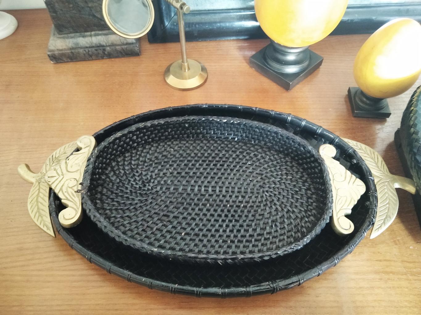 Black rattan trays and brass handles of oriental origin 3 pieces. Mid 20th Century

 The lot of oriental trays of Ratan and Brass consists of two oval trays with side handles and a tray also made of rattan with handles in the form of a bowl or