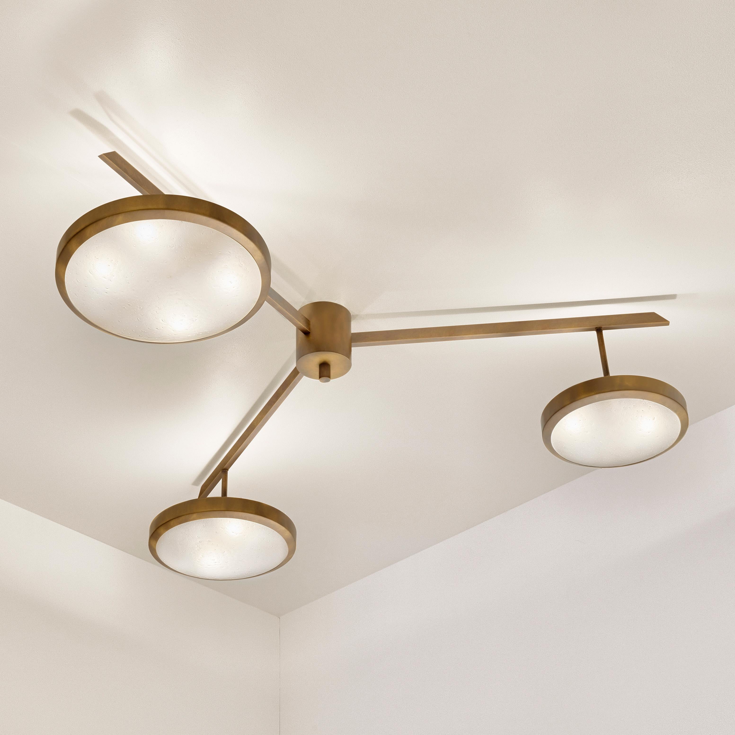 The Tre ceiling light harmoniously juxtaposes the balance of its three evenly spaced arms with the asymmetry of its variable size shades staggered at different heights. The first images show the fixture in our bronzo nuvolato (bronze)