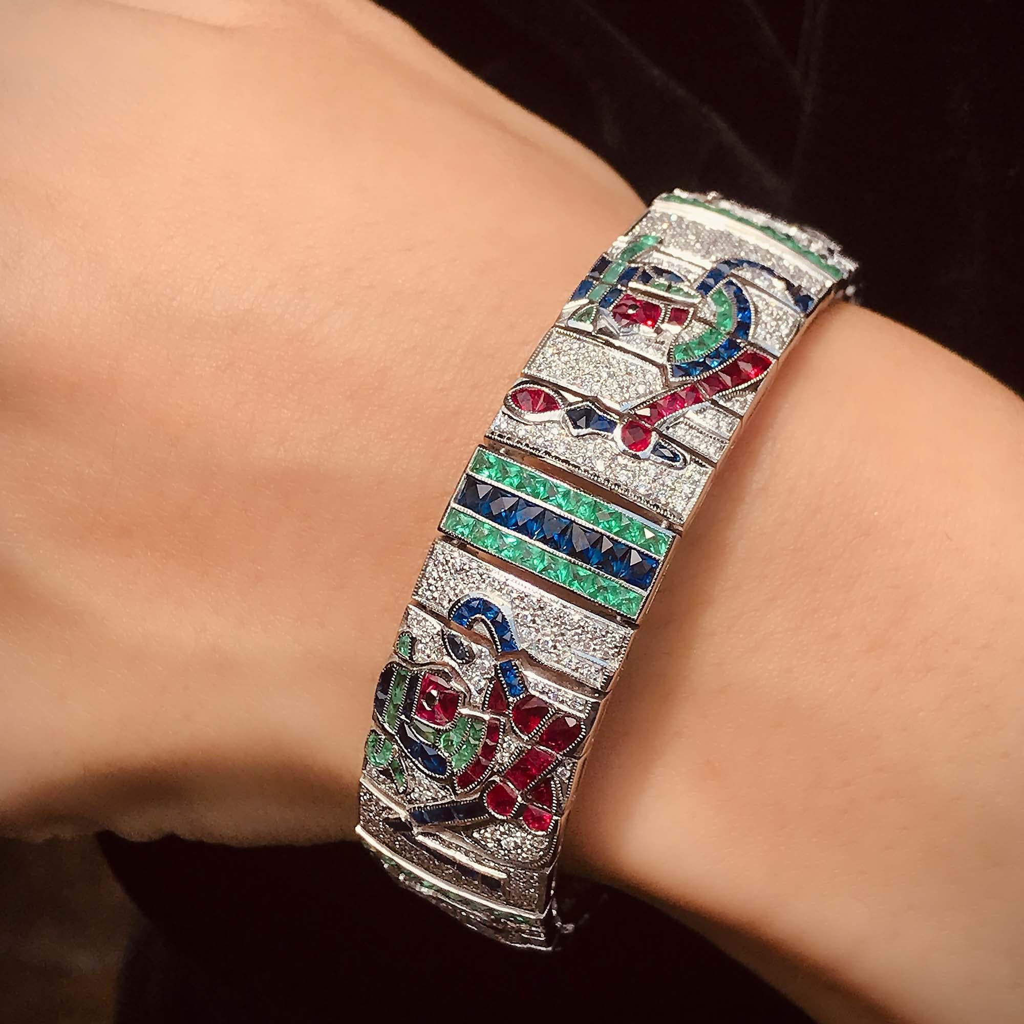 A rare and incredible Egyptian revival color gemstone and diamond wide bracelet. Compose of four main panels, each panel depicting ancient Egyptian symbols. The bracelet is adorned with diamonds, blue sapphires, rubies, and onyx. The Egyptian
