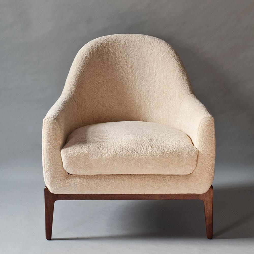 The Treble side or armchair by DeMuro Das has a curved profile supported by a three-legged solid walnut base. The chair is fully upholstered with a tight back and can be made in down-feather fill (feather and down wrapped around a foam core) or