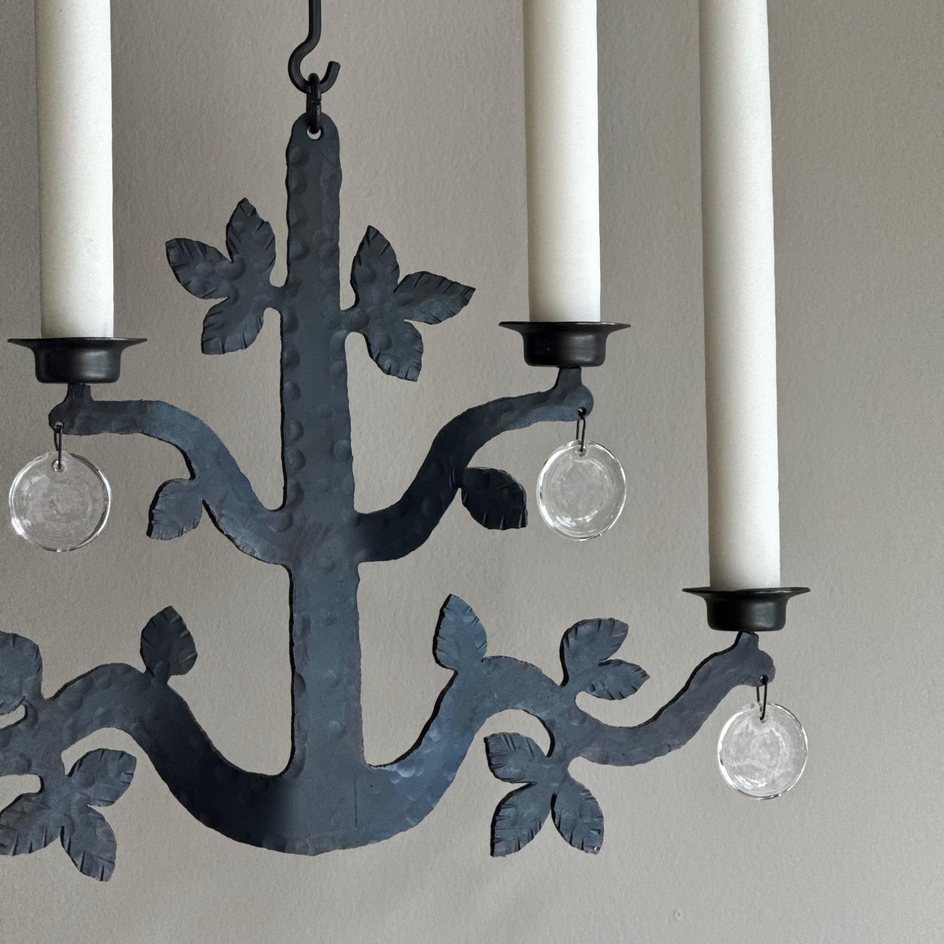 A four-armed, iron and glass chandelier designed by Bertil Vallien for one of the leading glass manufacturers in Sweden during the mid-20th century, Boda Smide. 

The hammered, vegetal form of this substantial wrought iron chandelier is indicative
