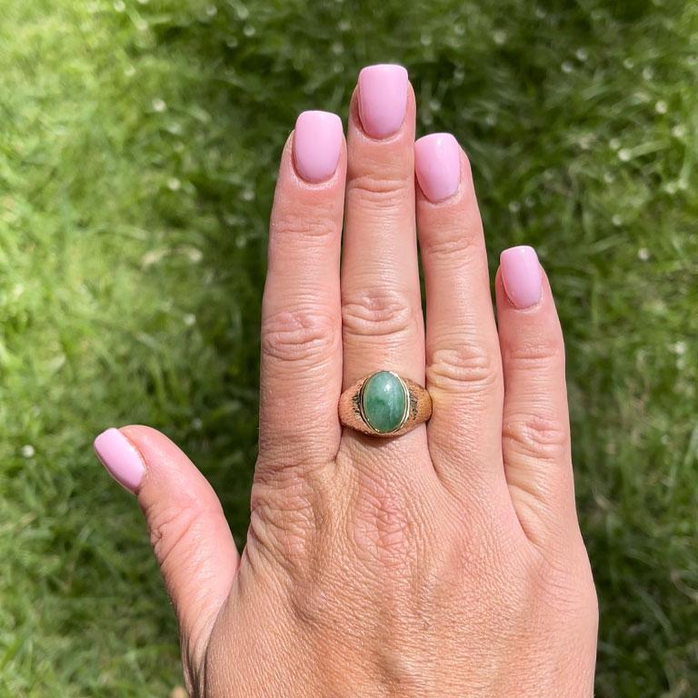 Oval shape cabochon green jade ring, bezel set in 14k yellow gold. The Jade measures approximately 14.10 mm x 10.11 mm x 5.02 mm with an estimated weight of 6.45 carats. The ring has a rounded tapered shank with tree-bark textured shoulders, and the