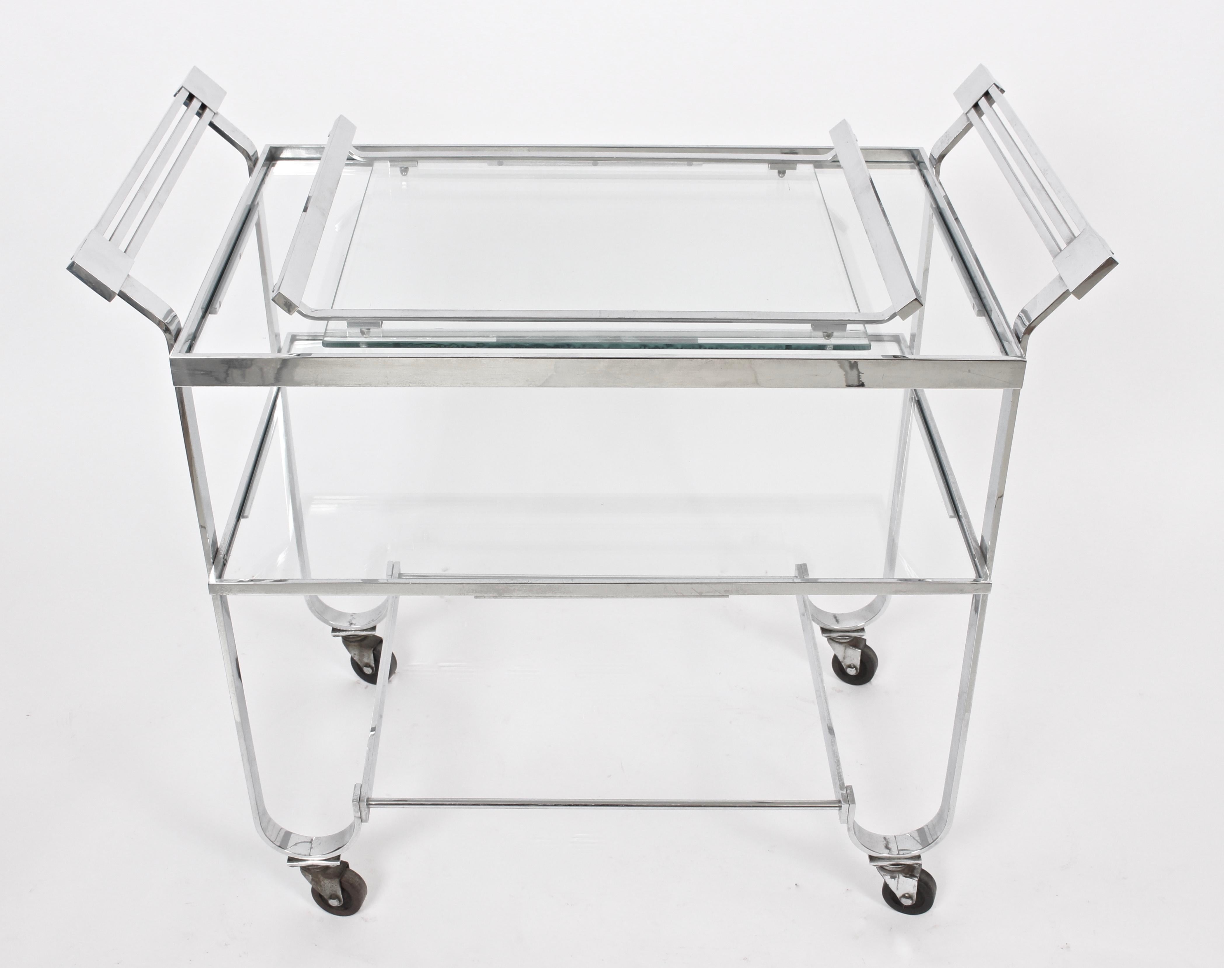 Classic Treitel-Gratz New York Art Deco bar cart - tea trolley - serving cart with removable lower serving tray. Featuring a lipped rectangular chrome frame with casters and three recessed glass shelves. Measures: 24.5 H to top shelf. Treitel-Gratz