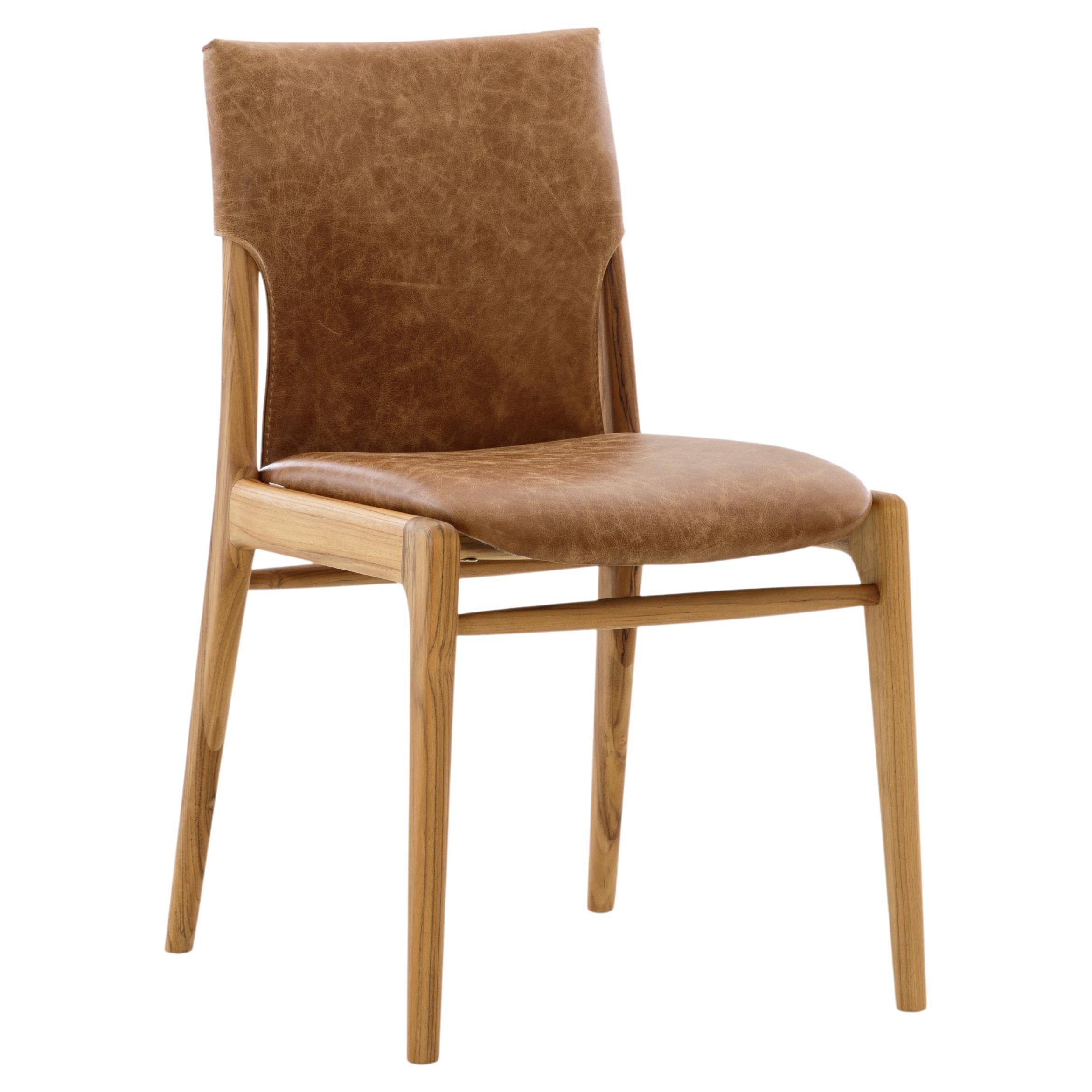 A pair of Tress teak wood dining chairs with distressed caramel leather. The Tress dining chairs blend refined elegance, durability, and exceptional craftsmanship, making them a sophisticated addition to any dining space. Designed with a strong,