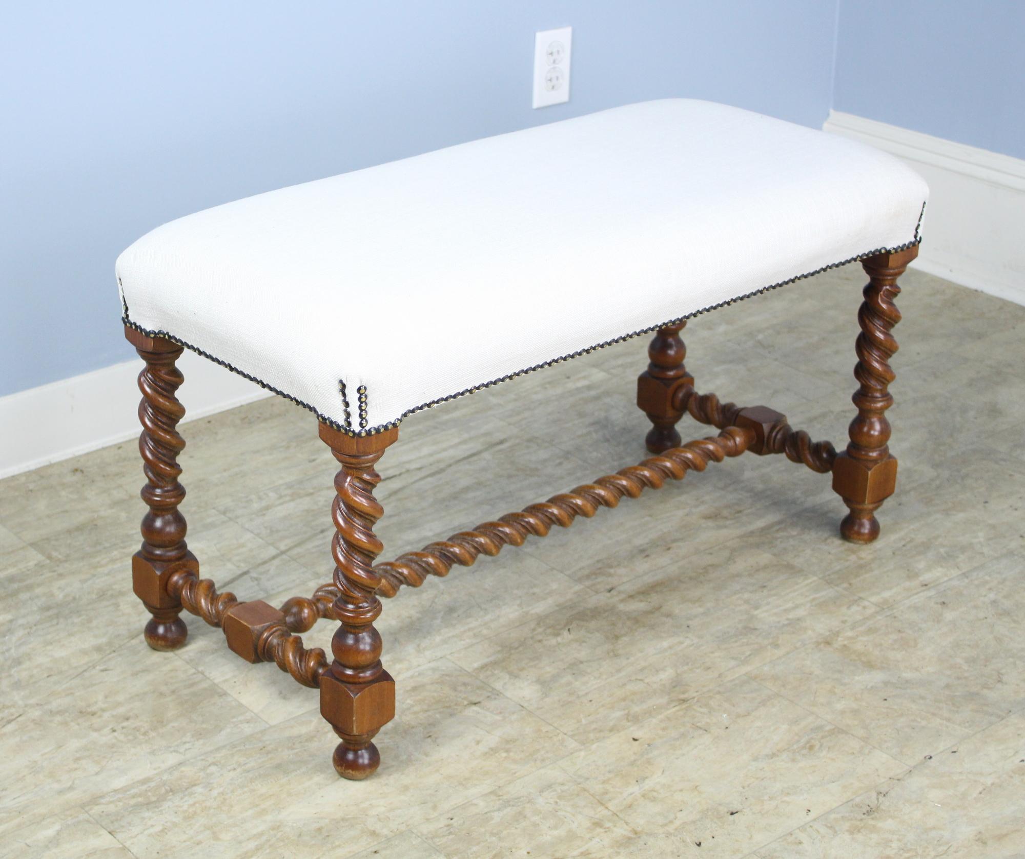 A stool or bench with visually arresting oak barley twist supports. Good nailhead detail where the seat meets the legs. Newly upholstered in white muslin to be used as is or reupholstered. Charming!