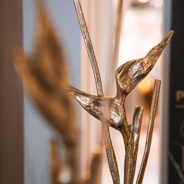 Die Tria-Skulptur ist eine bemerkenswerte Verschmelzung von botanischer Eleganz und raffinierter Handwerkskunst. Sie besteht aus zarten, handgefertigten tropischen Helikonien, die sich anmutig aus einem Sockel aus Naturstein erheben. Jedes Element