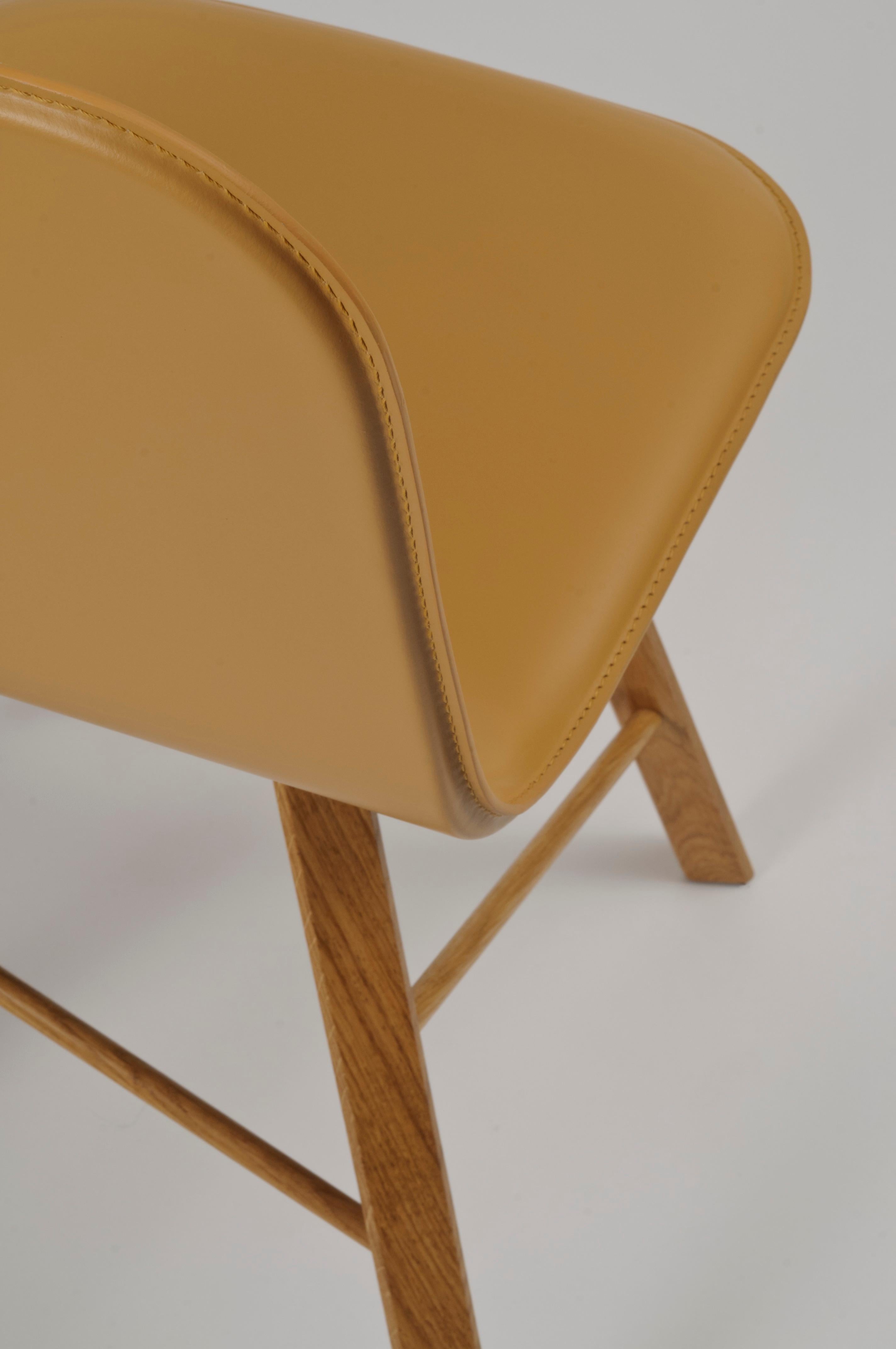 Essential and elegant chair with a bent plywood shell, and four iconic legs with triangular shape in solid oak, joined by transversal wooden bars.
The shel is upholstered in natural leather available also in black and other different colors. In