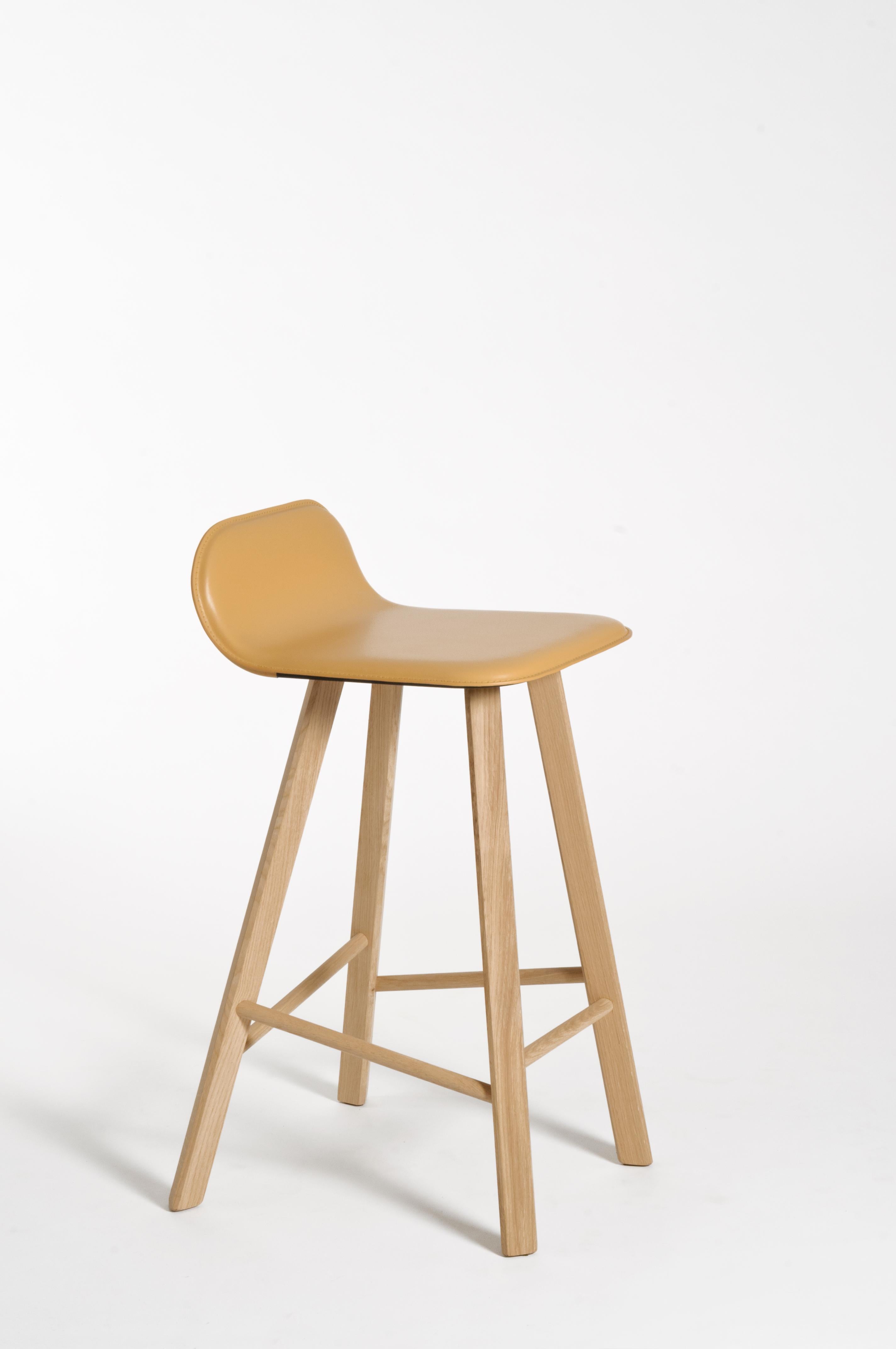 Essential and elegant stool with a bent plywood shell upholstered in leather. and four iconic legs with triangular shape in solid oak, joined by transversal wooden bars. The seat can have a low back as listed, or an high back as a normal chair for a