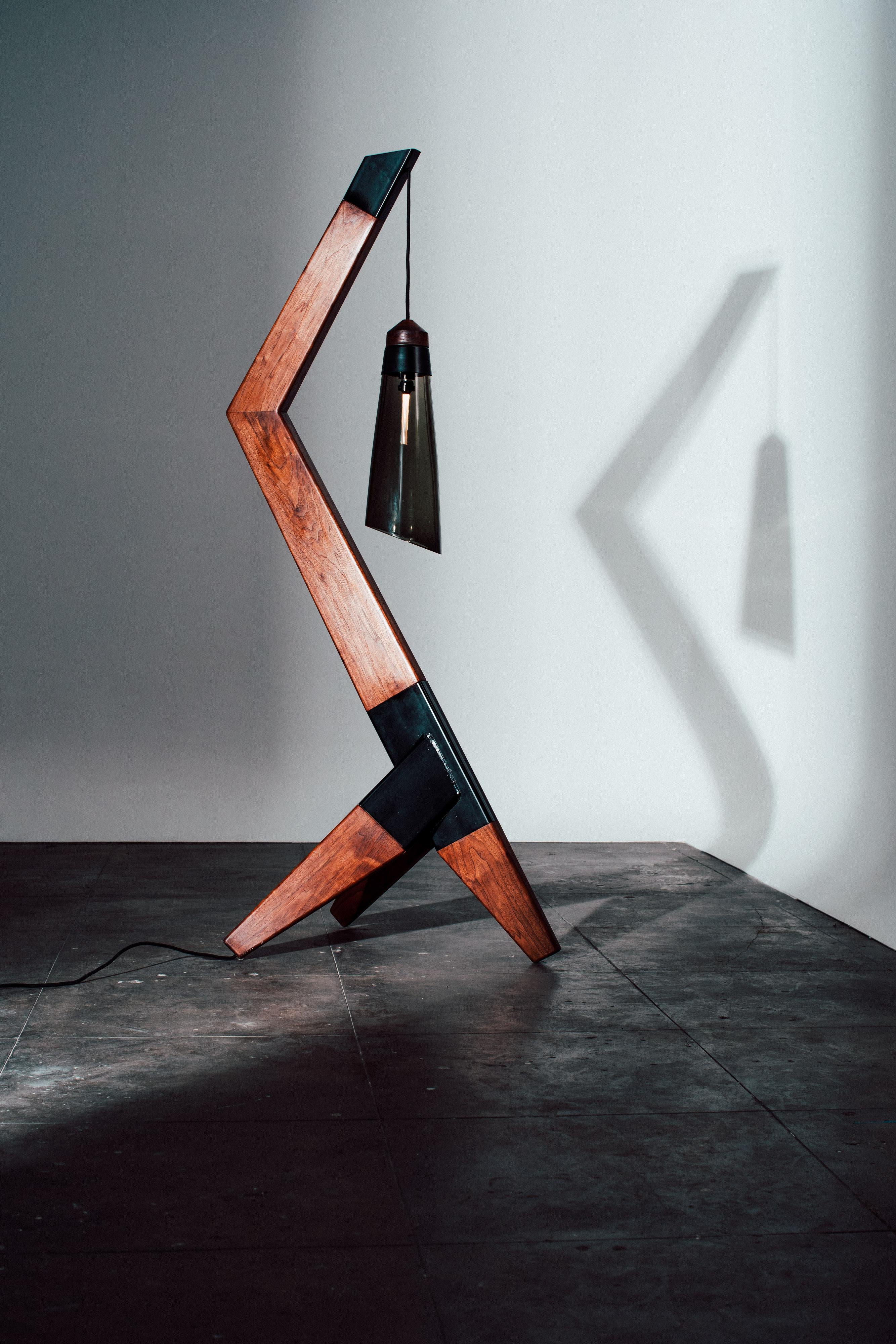 Floor standing lamp shown in walnut, steel, and hand blown smoked glass. This pieces was developed in our early collections and has stood the test of time. The angles and materials are a beautiful combination to witness. 
 