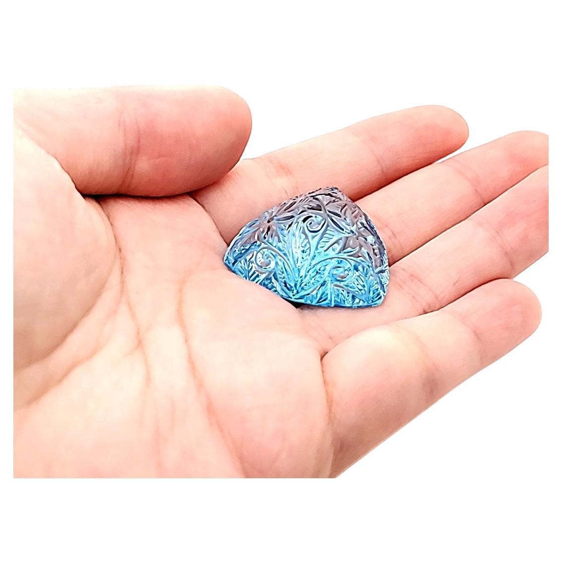 Questa gemma unica da 70,14 carati affascina con le sue sfumature blu intenso, che ricordano le acque cristalline dell'oceano. 

L'intaglio artistico delle foglie aggiunge un fascino tropicale, trasformando questo topazio in un tesoro vibrante e