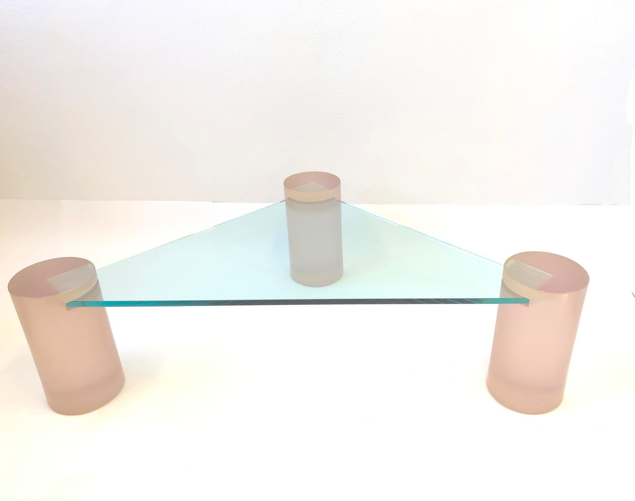 Glamorous 1980s triangular blush pink satin Lucite and glass cocktail table in the style of Karl Springer.
The table is constructed of three solid satin Lucite 8.75” diameter cylinders and 3/4” thick glass top. The glass slides in to each leg. New