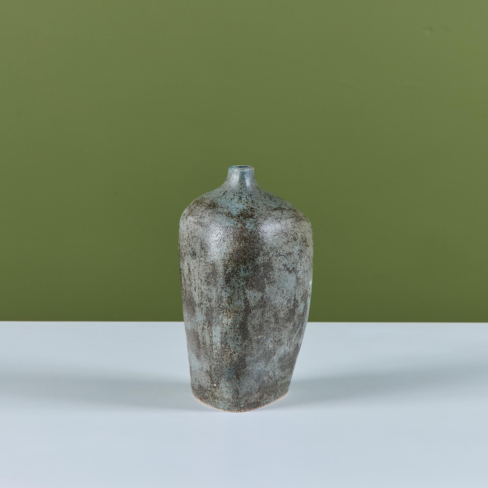 Vase triangulaire en céramique émaillée avec des coins arrondis. Le vase en forme de bourgeon présente une glaçure bleue et brune mouchetée et une petite embouchure triangulaire. Signé au verso.

Dimensions
6