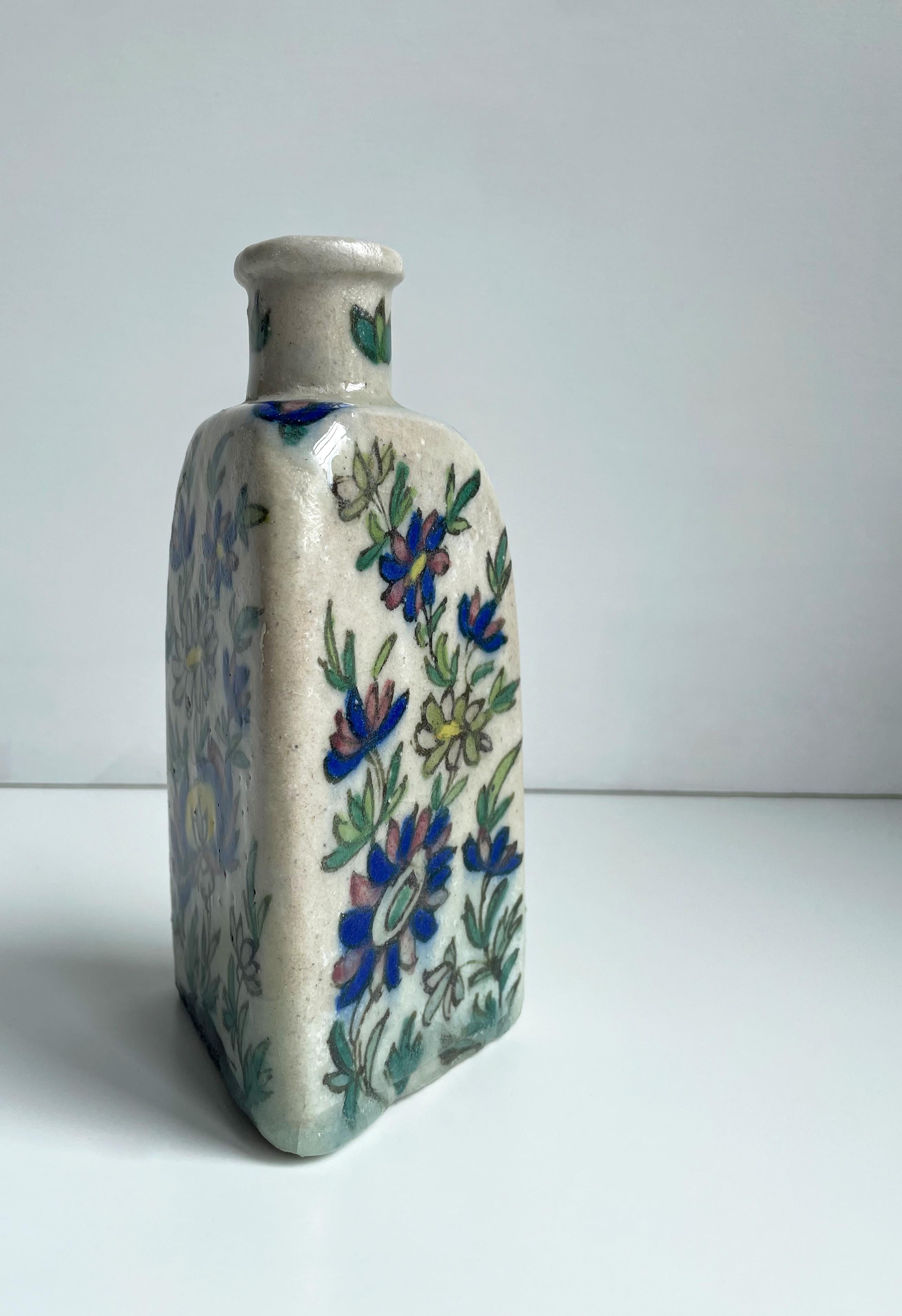 A magnificent triangular Middle Eastern antique handmade ceramic tea bottle with hand painted highly colorful decor and clear glaze. Light and dark green, red, yellow and admiral blue organic floral decorations on a greyish white base with clear