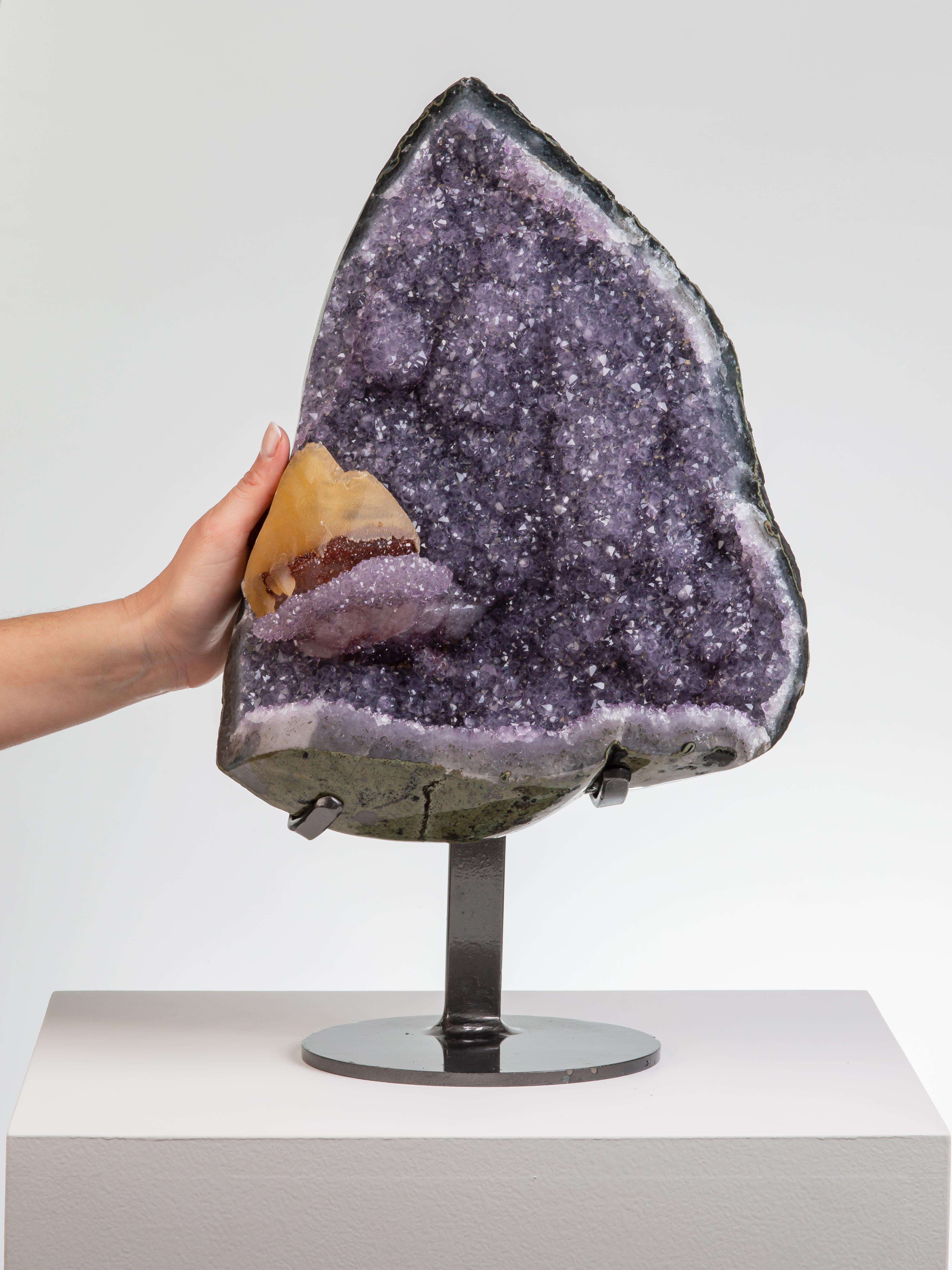 A beautiful triangular geode section in lilac amethyst with a gold coloured
calcite perched on a bed of red druzy quartz.

This piece was legally and ethically sourced directly in the prestigious mines of Uruguay, South America. Uruguayan