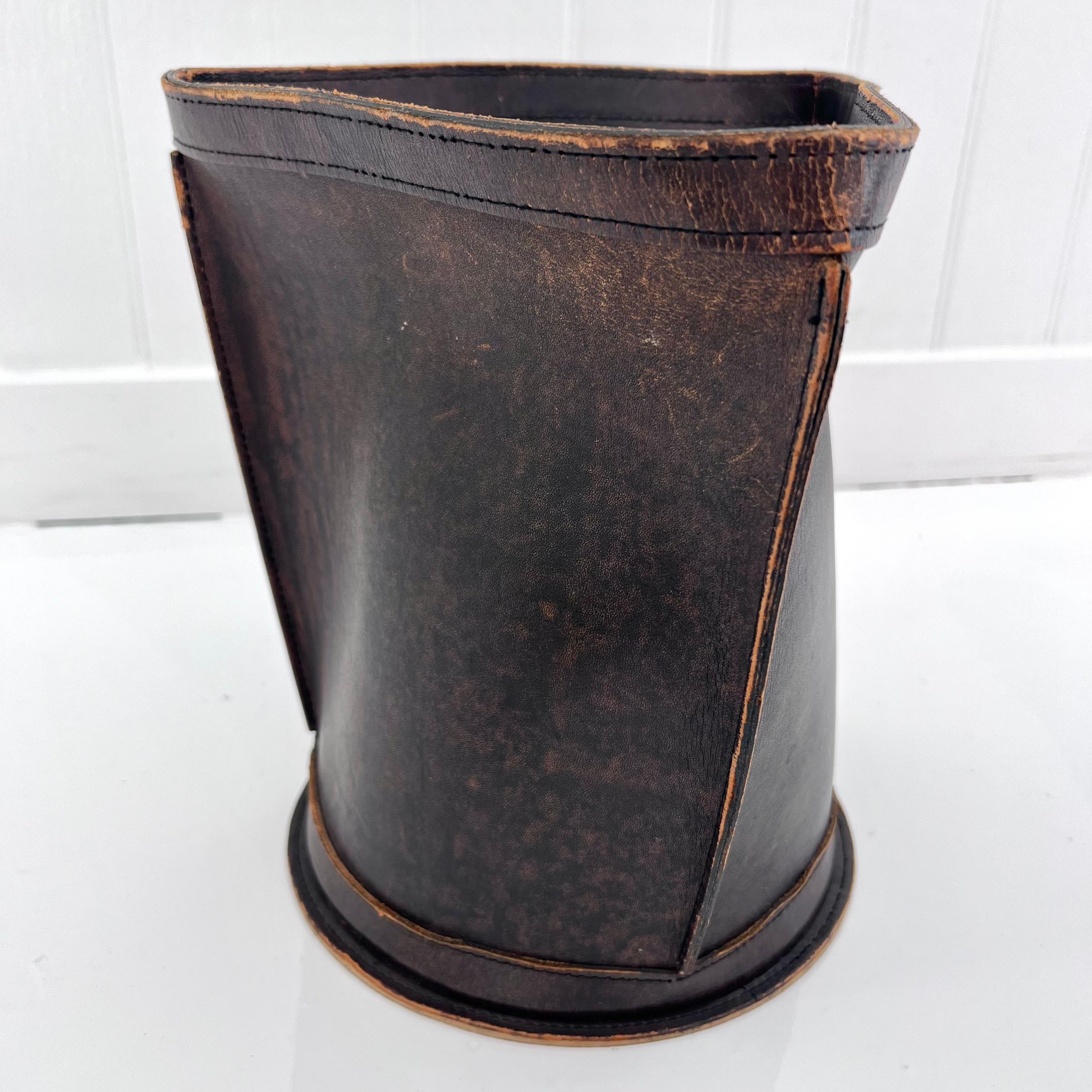 Beautiful distressed leather waste bin. Fully made of a thick cowhide leather with the upper stitched in a triangular shape and fastened onto a circular base giving it great lines. Great rich brown color with tan brown undertones. High quality