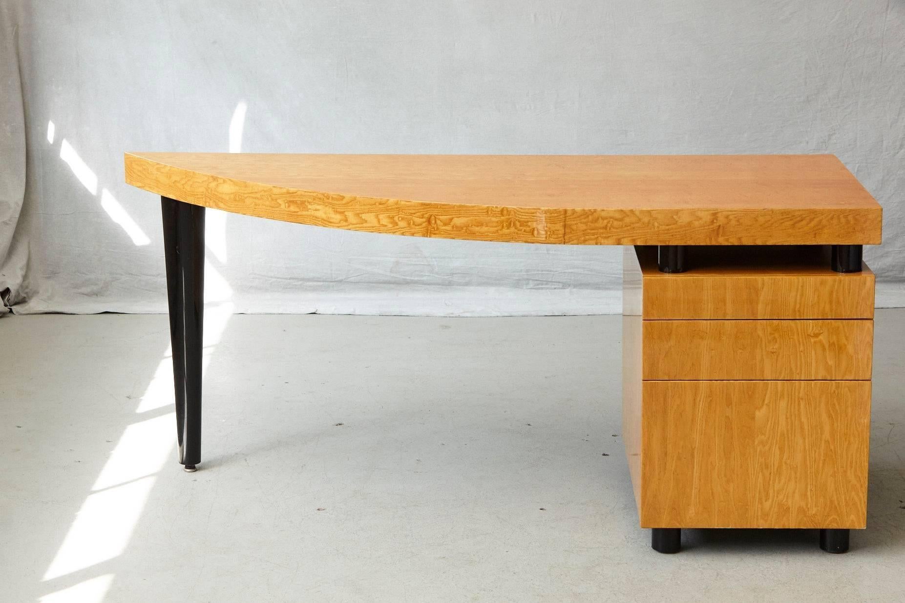 Triangular, almost sail-shaped desk in high gloss lacquered walnut with three drawers. The desk is mounted on cylindrical black lacquered legs, with one prominent tapered black lacquered leg.

There are two flaws along the edge, which are