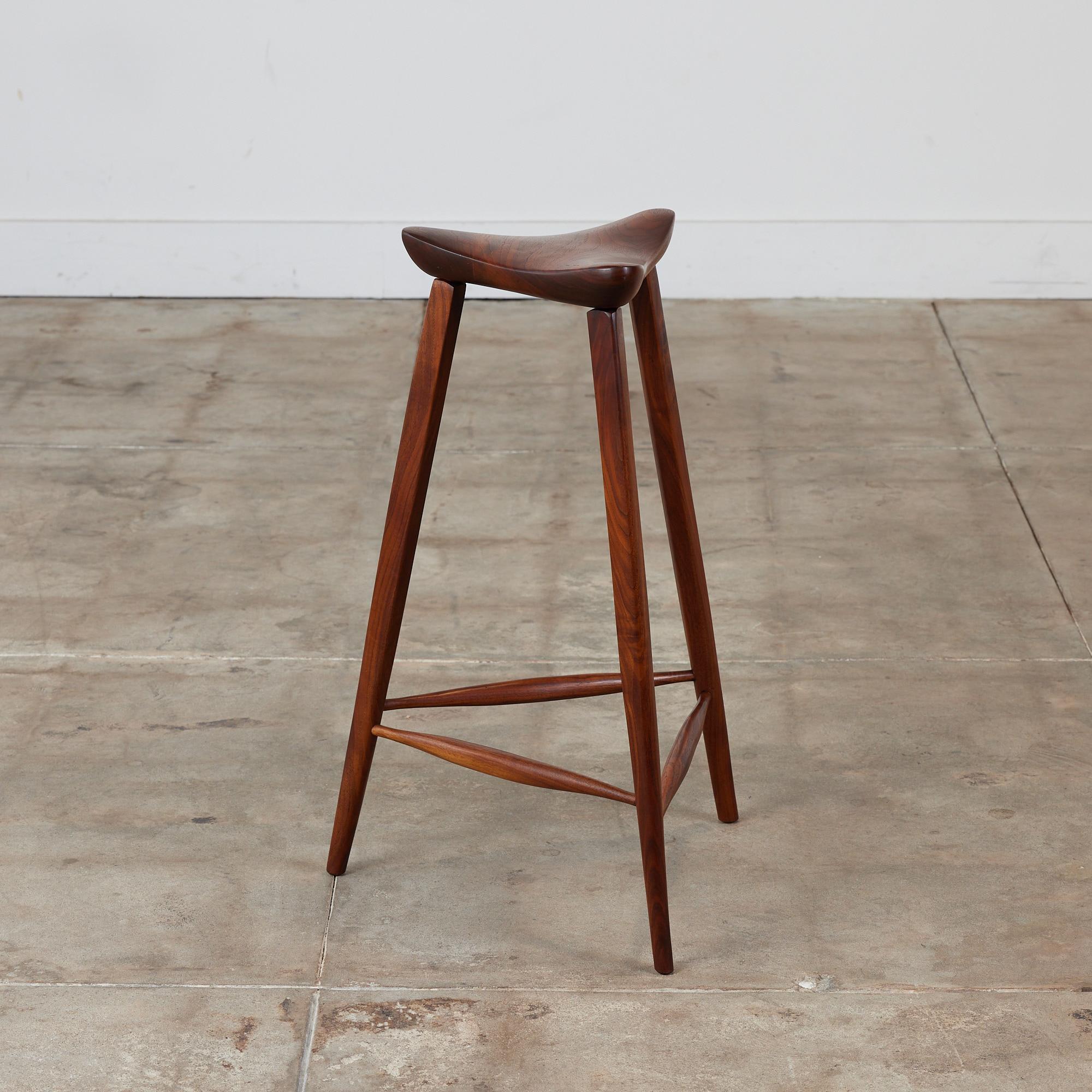 Triangular studio craft stool made in 1979. The walnut stool showcases a minimalist design with a triangular seat with soft edges and corners that slightly turn upwards. The stool is supported by three tapered dowel legs with stretchers.

Signed