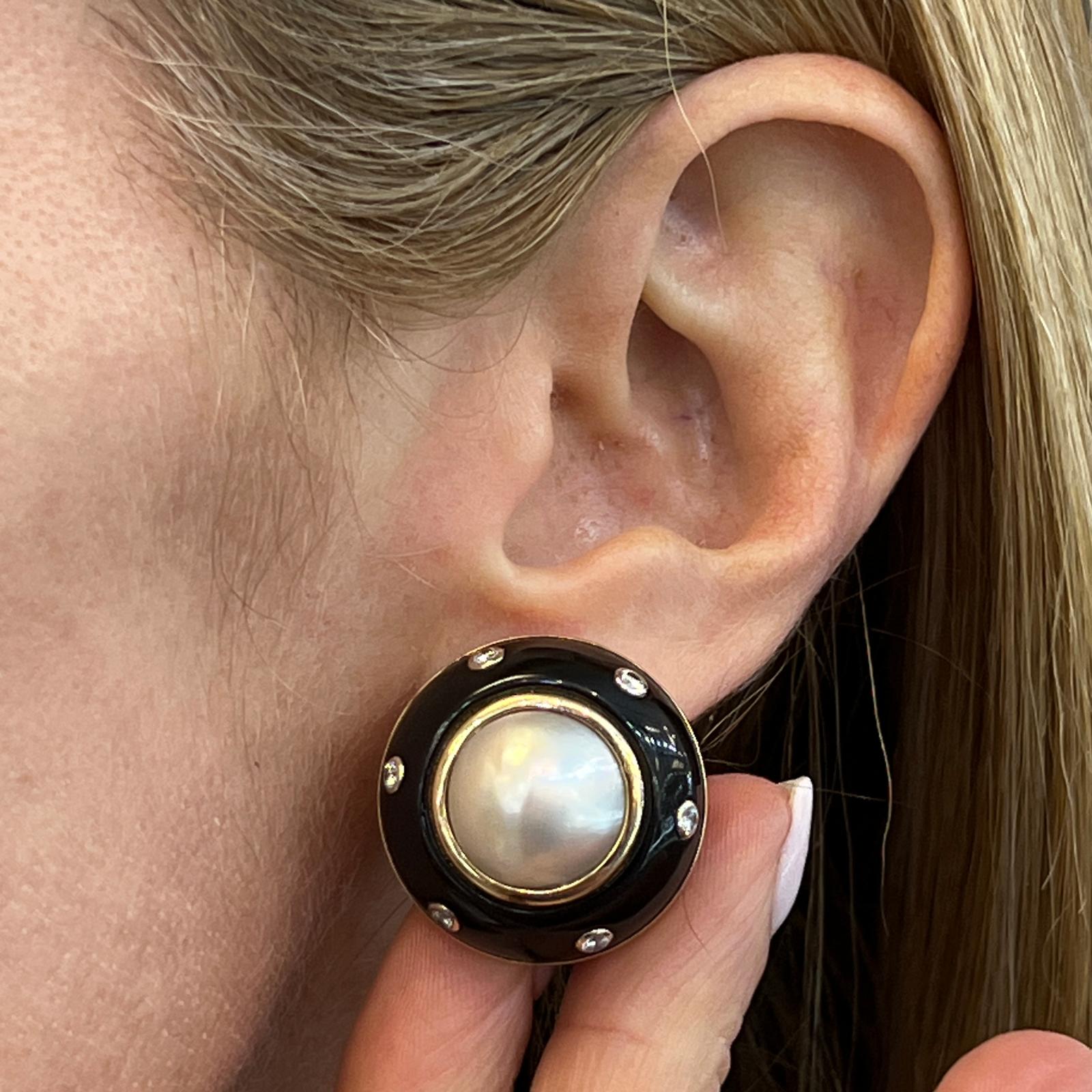 Circular-shaped cabochon earrings, each earring centering a larger mabe pearl with 12 round-cut diamond accents, in 14k yellow gold, and stamped Trianon. The earrings measure 1.0 inch in diameter. 