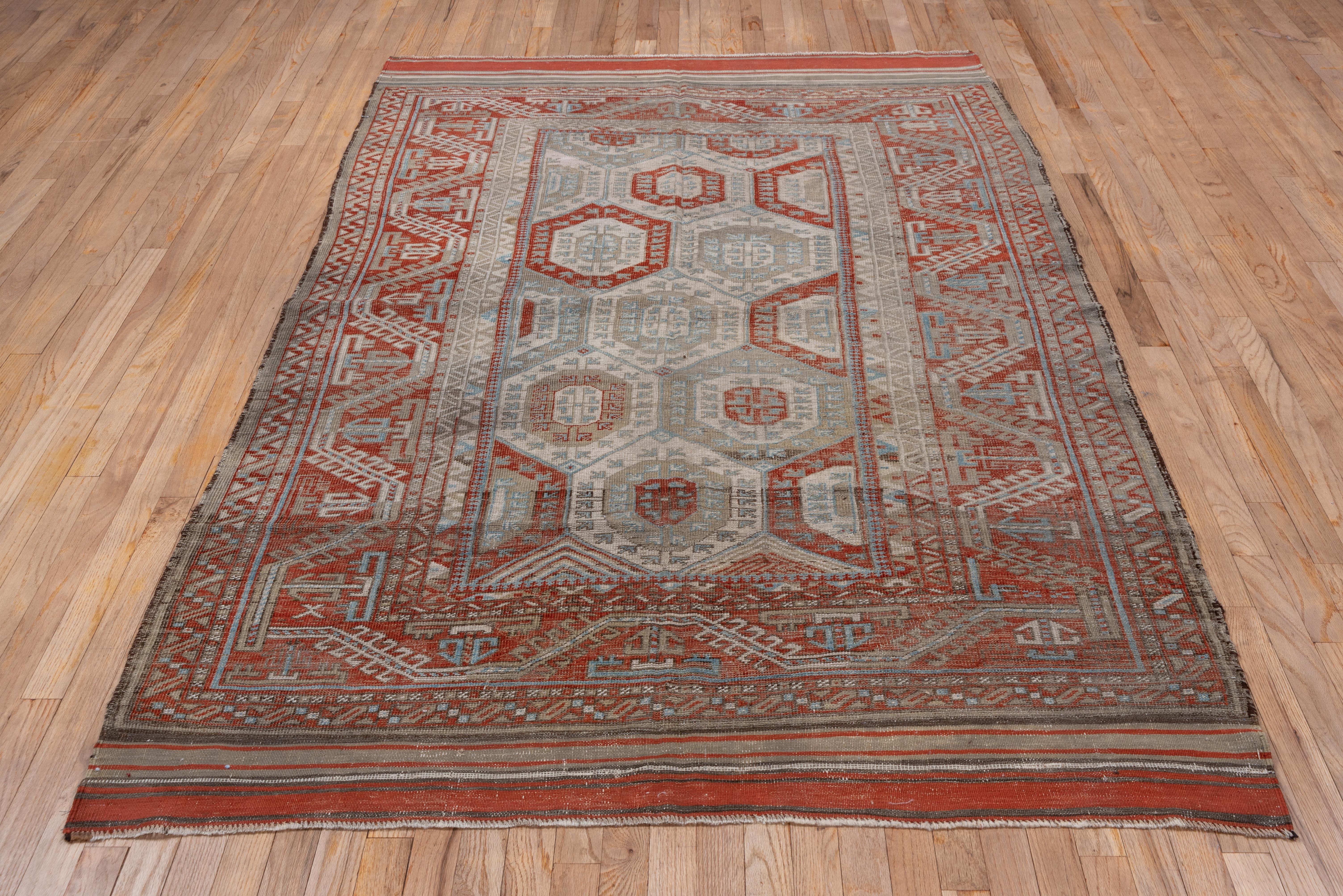 A Turkmen-style faceted undulating hooked vine and palmette border closely frames a repeating pattern of layered hexagons enclosing and sprouting small flowers, accented in shades of red, mauve and graphite. This east Persian/West Afghanistan large