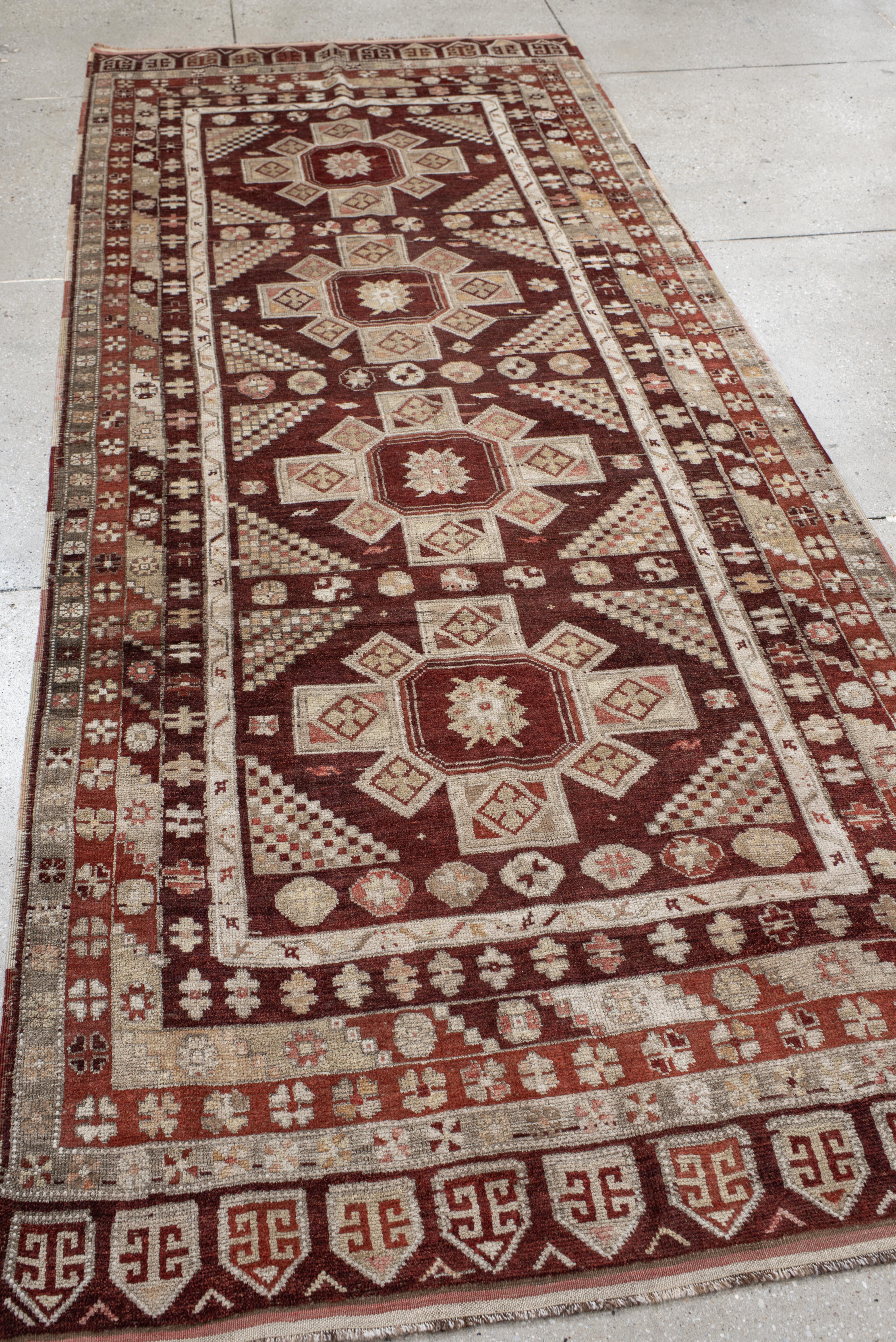 Questo tappeto vintage anatolico annodato a mano presenta un'imponente composizione tribale incentrata su medaglioni a forma di croce disposti in una griglia geometrica. Il campo rosso scuro contrasta elegantemente con gli accenti in avorio, pietra