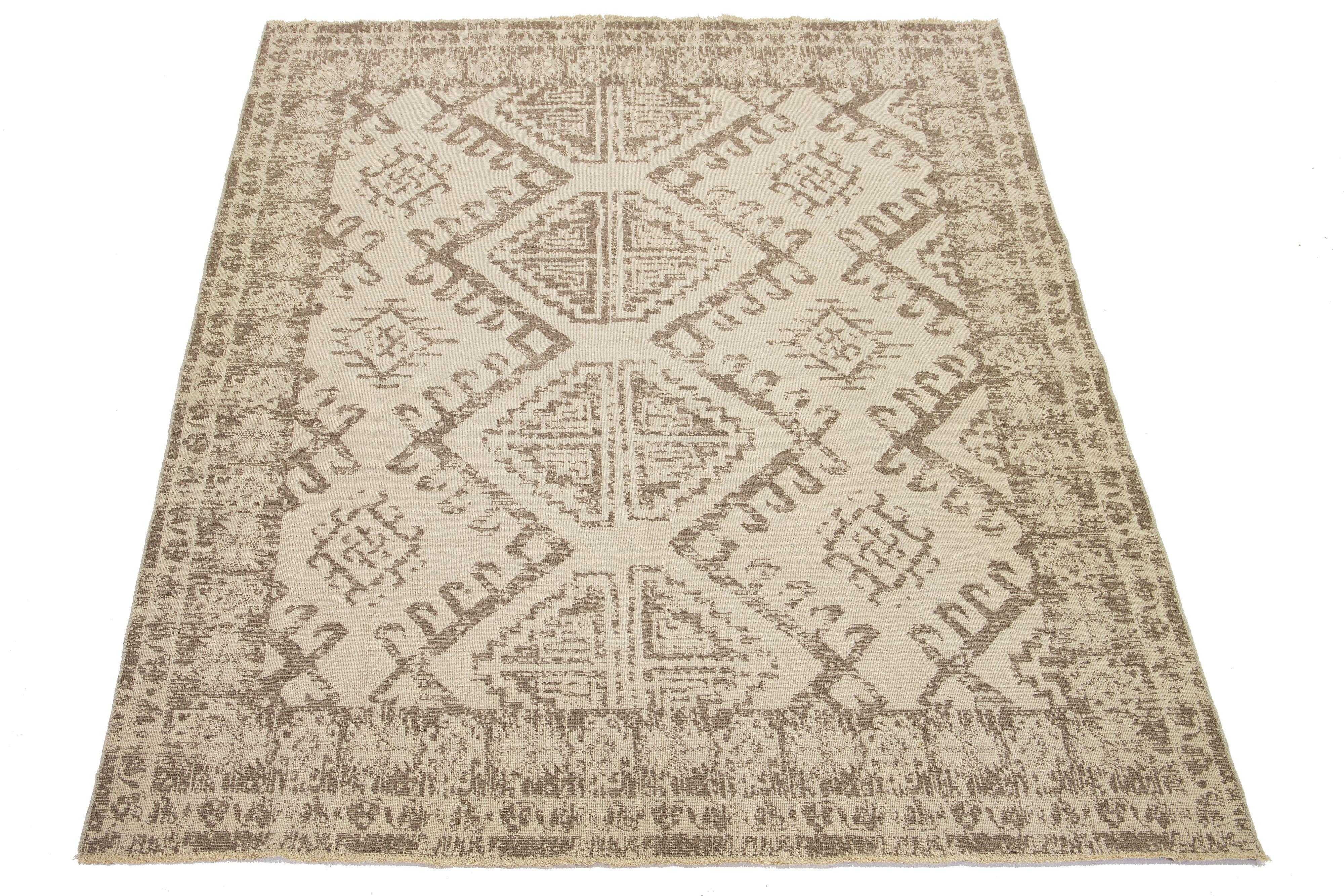 This hand-loomed wool rug features a beautiful beige background with a tribal pattern in brown that covers the entire rug. 

This rug measures 9'8