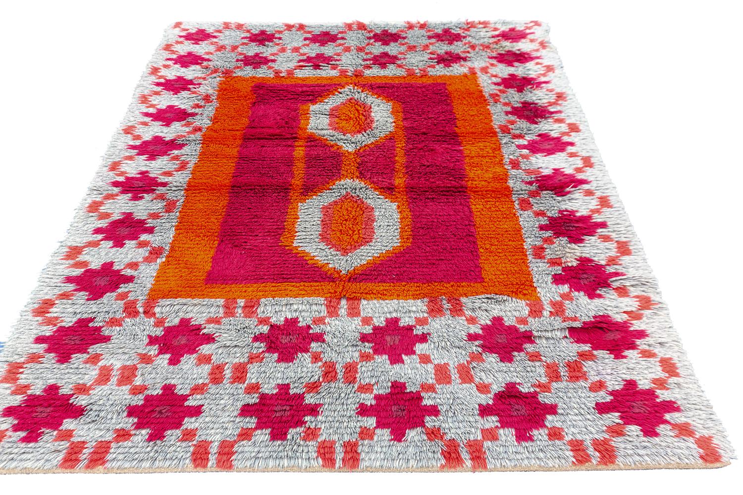 This is a vintage Swedish “Rya” rug woven circa 1950-1970 that measures 200 x 144cm. It has a tribal field design with a center geometric diamond medallion motif enclosed within a red and orange square. The background of the rug is composed of a