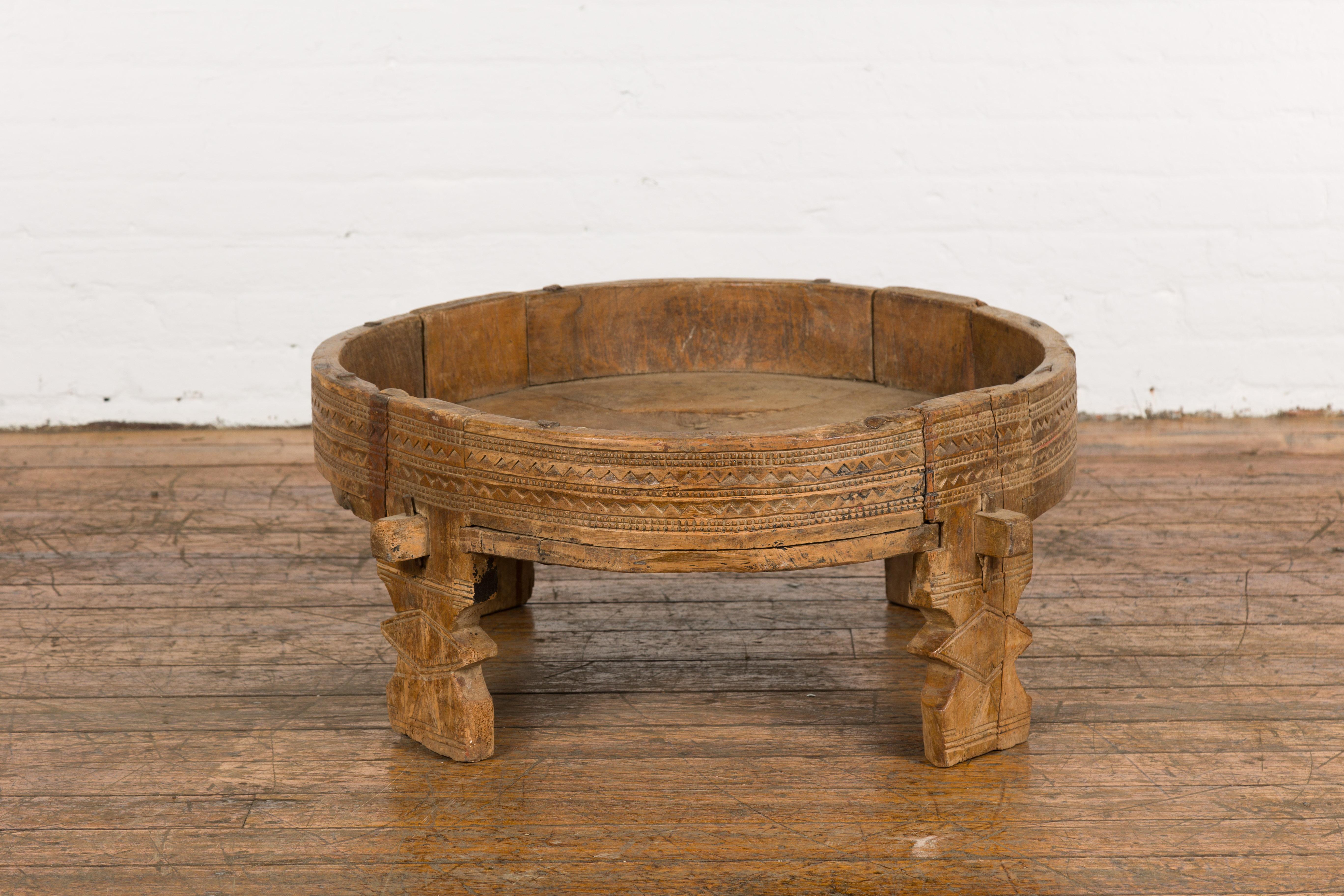 A Tribal Indian rustic teak wood Chakki grinder table from the 1920s with hand-carved geometric motifs, open center, carved feet and weathered patina. Discover the enchanting allure of this tribal Indian rustic teak wood Chakki grinder table from
