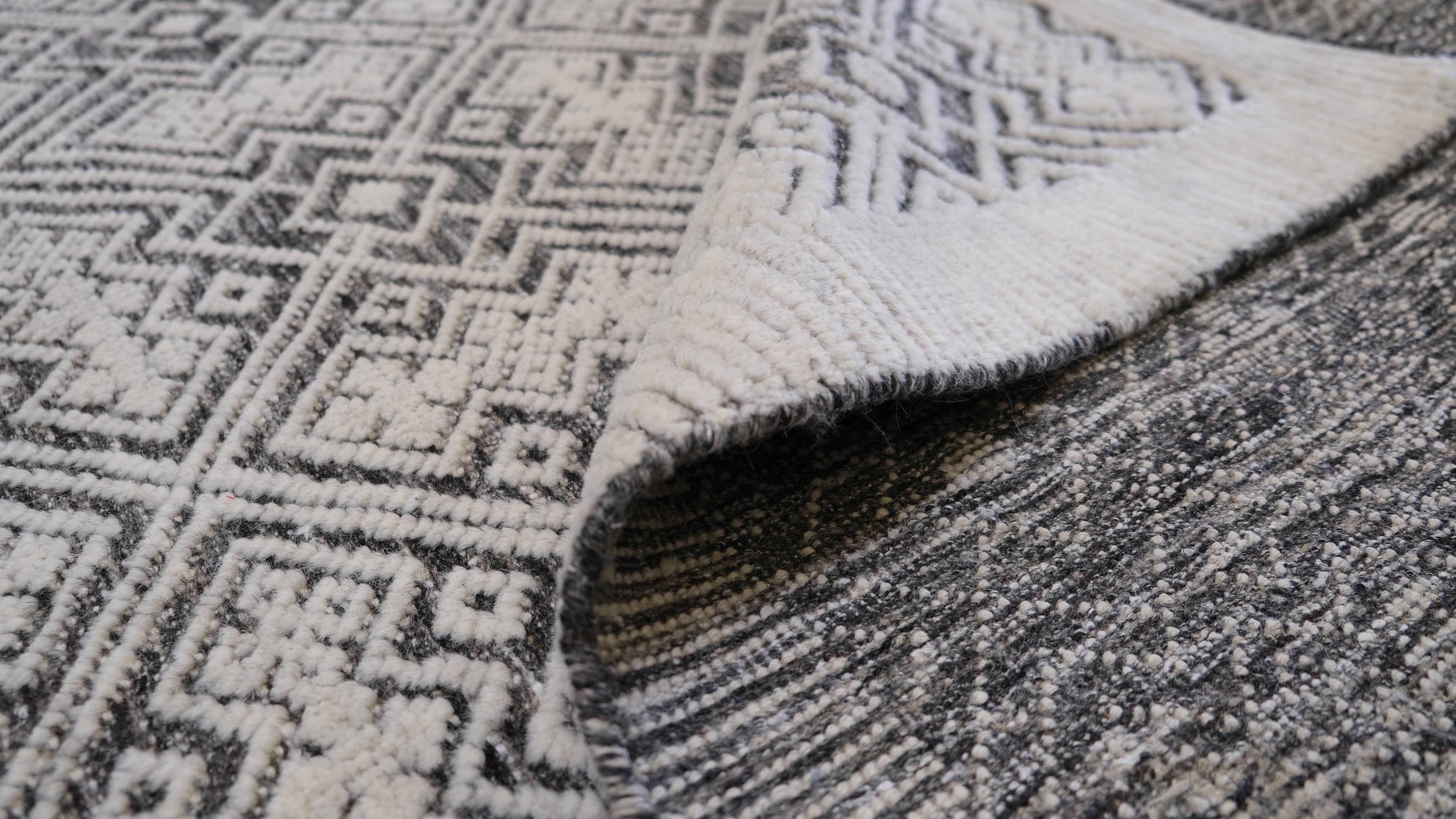 This hand-knotted wool rug showcases an intricate gray and white tribal-inspired geometric pattern, adding depth and visual interest to any space. The detailed diamond lattice design, composed of finely woven symmetrical motifs, creates a textured,
