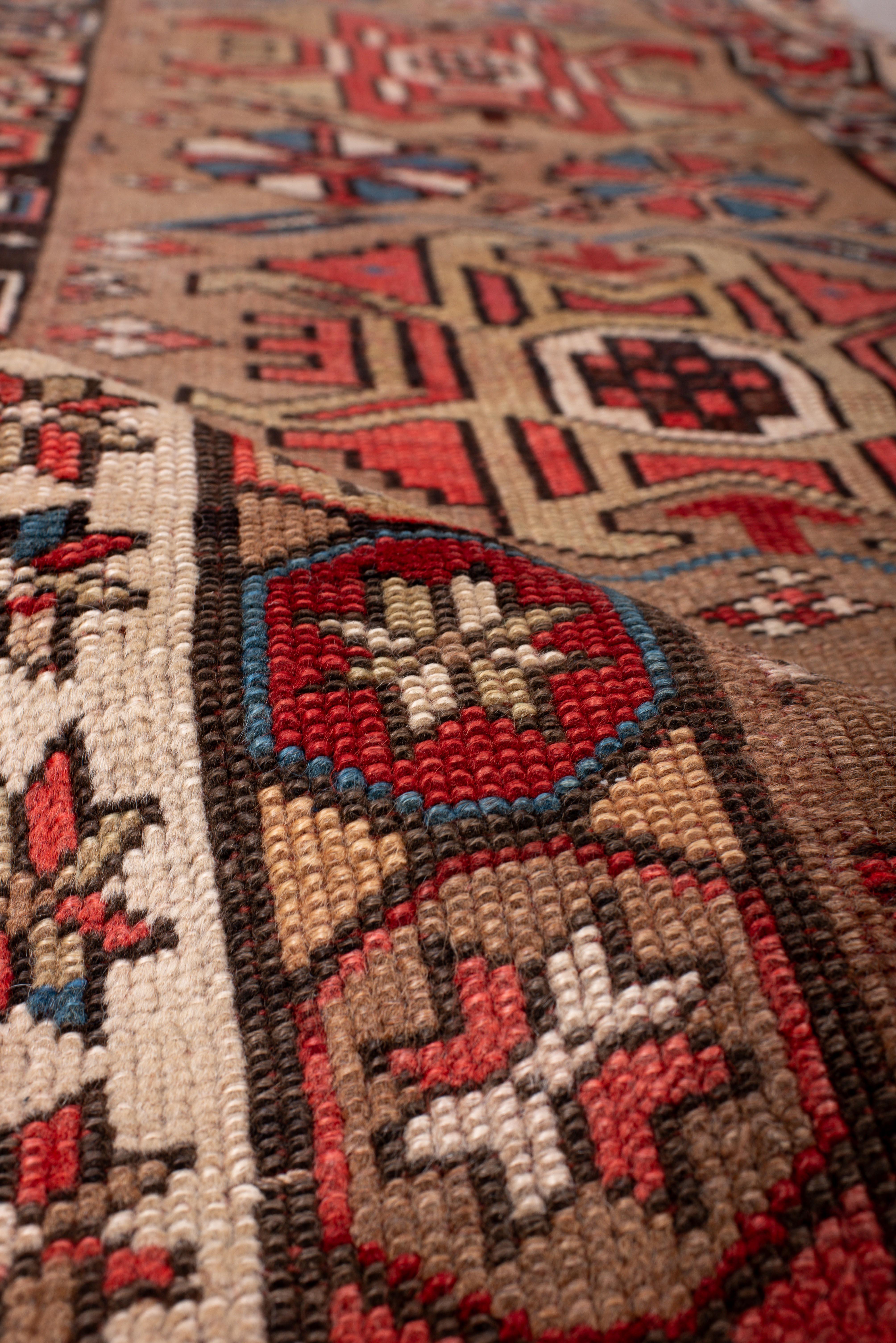 Ce remarquable chemin de table persan du nord-ouest présente une esthétique audacieuse inspirée du Karabagh, définie par un arrangement rythmique de médaillons angulaires et de rosettes florales stylisées. Sur un fond de couleur camel, le motif se