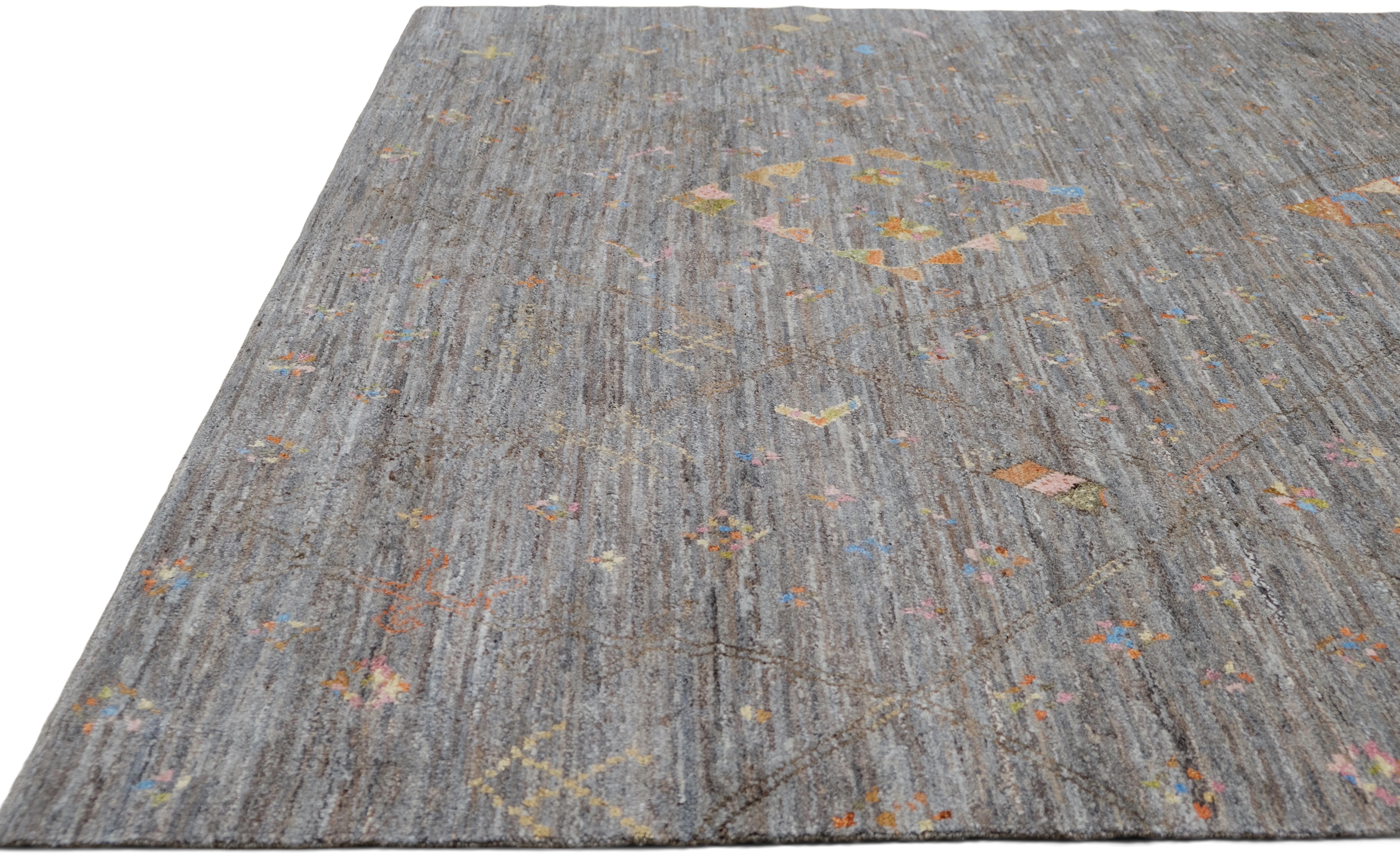 Esta impresionante alfombra de lana anudada a mano muestra la excepcional destreza de hábiles artesanos, mezclando motivos tribales tradicionales con moderna sofisticación. La suave base gris está adornada con delicados acentos geométricos en
