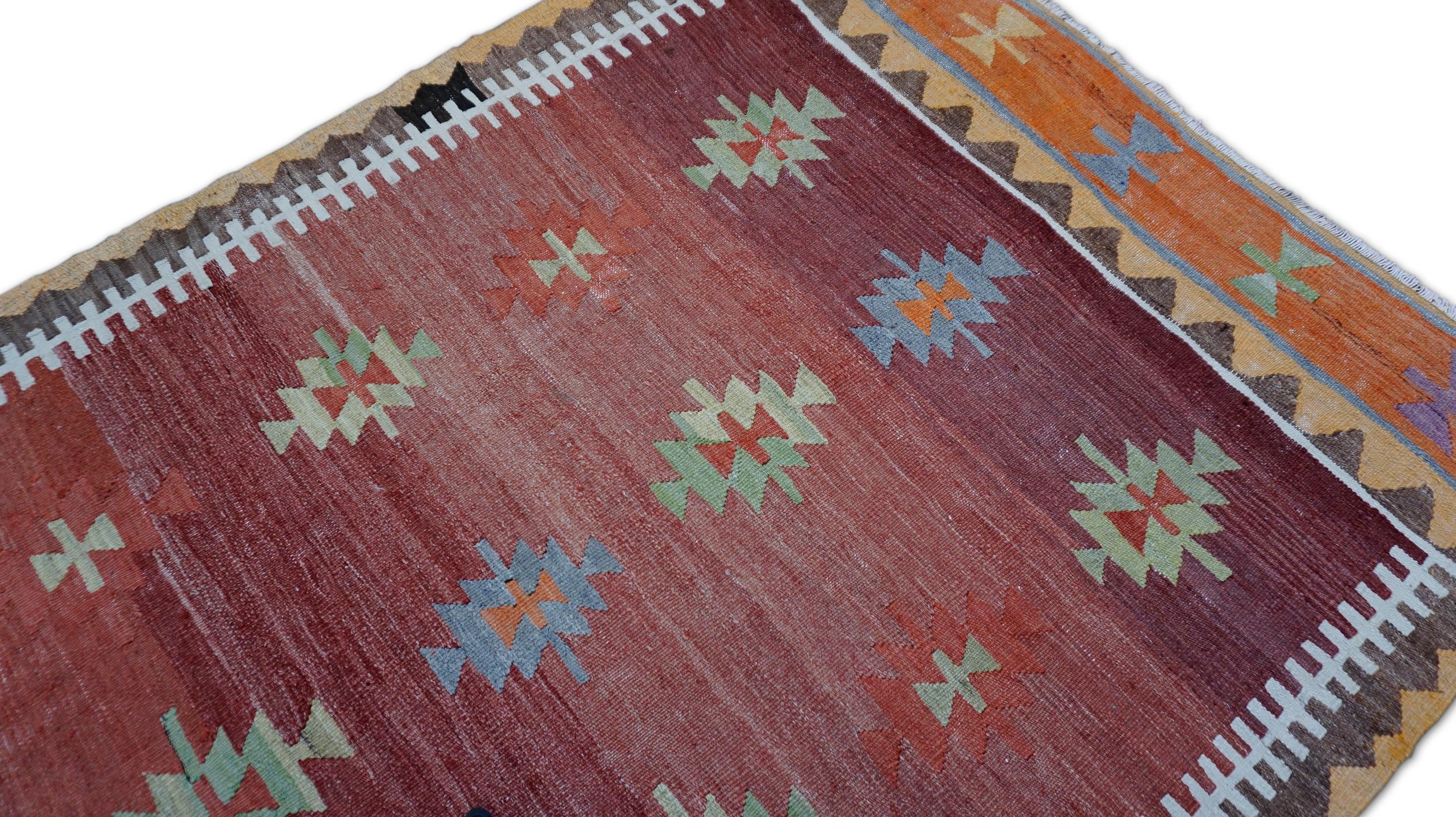 Este vibrante kilim vintage es un sorprendente ejemplo del arte tradicional del tejido plano. Tejido a mano con  de lana, la alfombra muestra un radiante campo rojo terracota salpicado de coloridos medallones tribales en verde, naranja quemado, azul