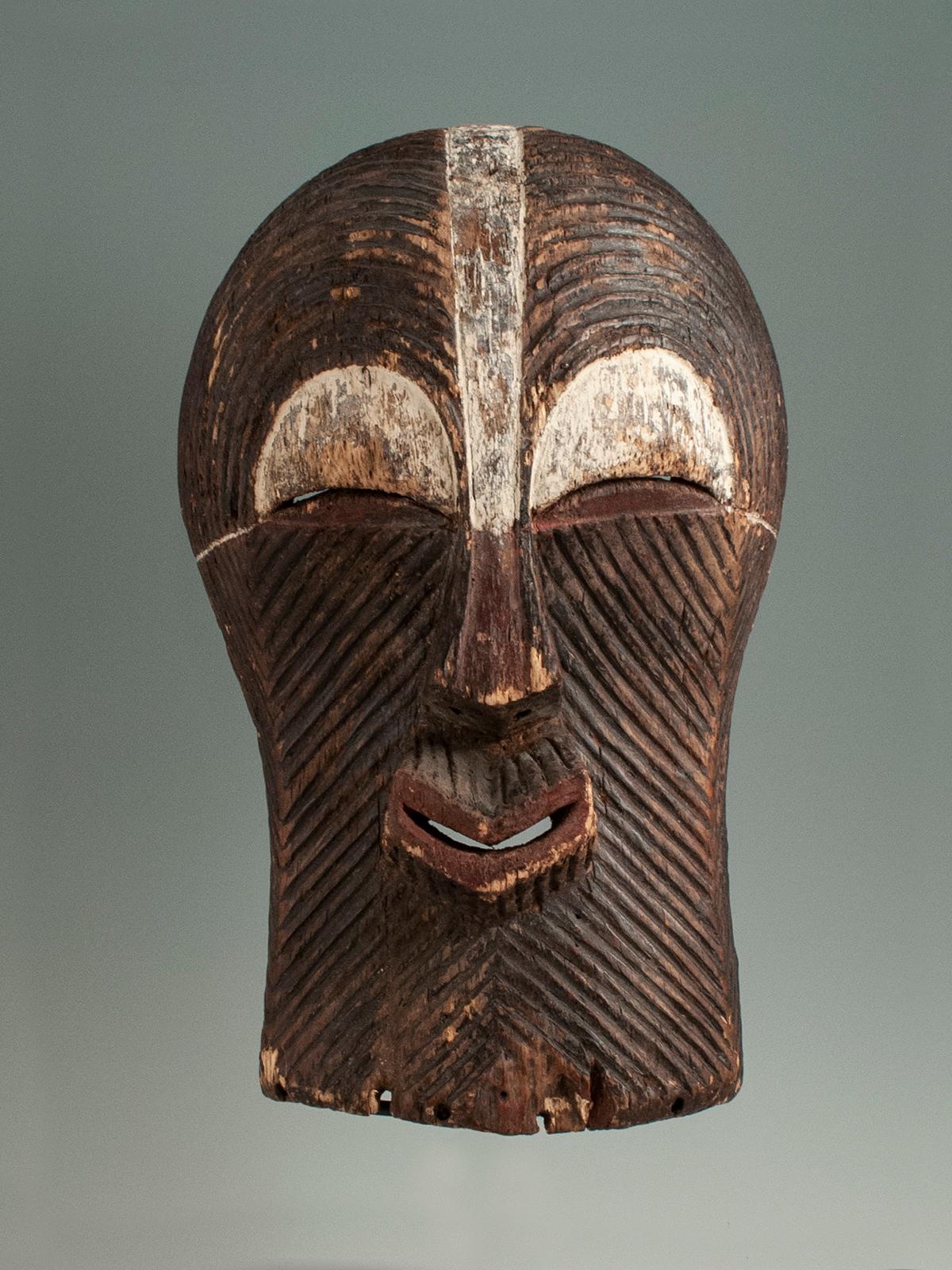 This graphic Songye Kifwebe mask has fine carved lines curved over the eyes and diagonal lines radiating from the nose and mouth in classic Kifwebe form. Mid-20th century mask from the Democratic Republic of Congo, central Africa. There are holes