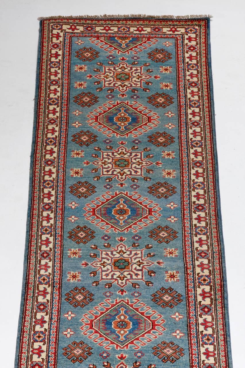 Dramatic Pakistani Runner Rug made in a Kazak style. Features a field of bold sky blue covered in geometric shapes. Multiple borders frame the field and the condition is excellent.