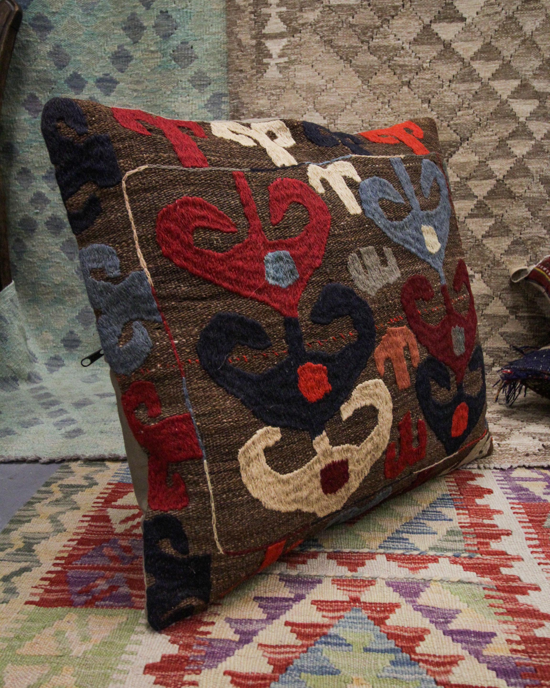 This truly unique tribal cushion cover is a larger piece suited to a bed or a sofa. Woven with a one of a kind repeating tribal motif pattern in accents of brown, beige, red and deep blue on a beige-brown background. This cushion's colour palette
