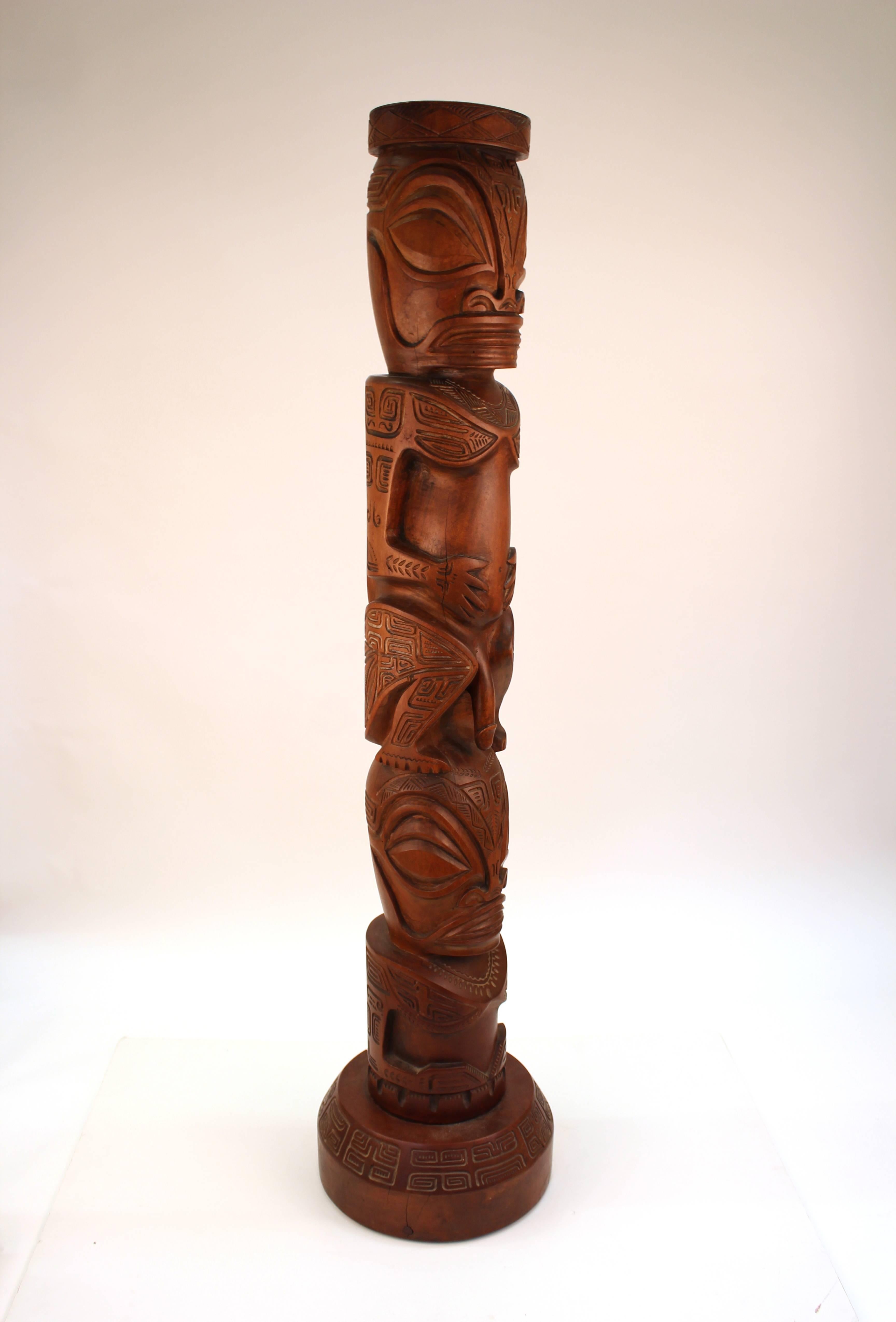 Decorative TOTEM sculpture after the style of the Marquesas Islands. Crafted in carved wood with a full nude human figure sitting atop another nude ending at the waist. The sculpture stands on around base and is intricately carved with geometric