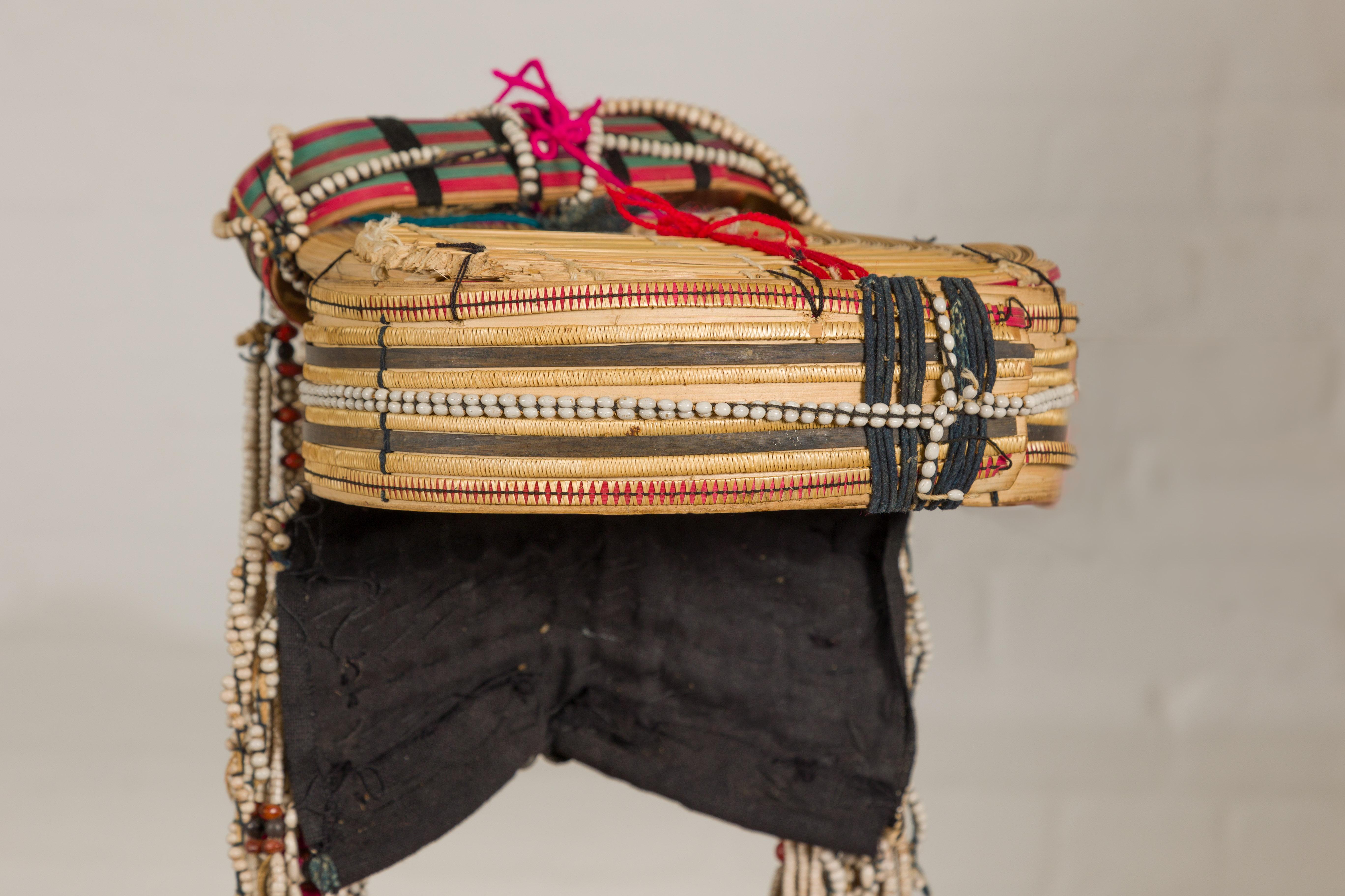 A Ulo Akha woman's Tribal headdress adorned with framework of bamboo, beads, pompons, seeds and other unique items. Experience a rich slice of the Akha tribe's vibrant culture with this exquisite Ulo Akha woman's tribal headdress. Traditionally