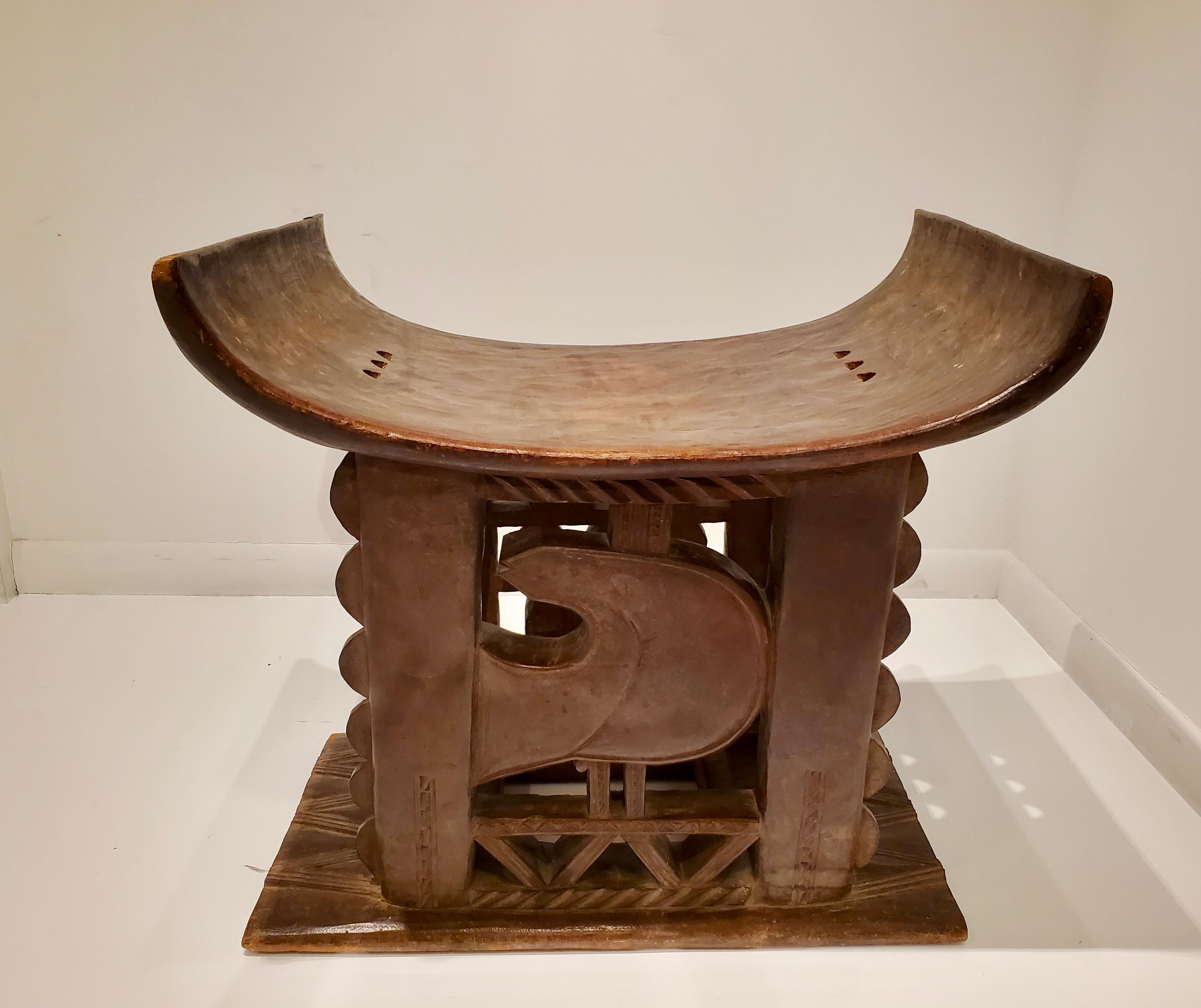 An exceptional and unusually large early 20th century African Ashanti hand-carved wood stool from Ghana featuring scalloped and geometric forms on one side with a stylized bird on the other which is the symbol of the word 
