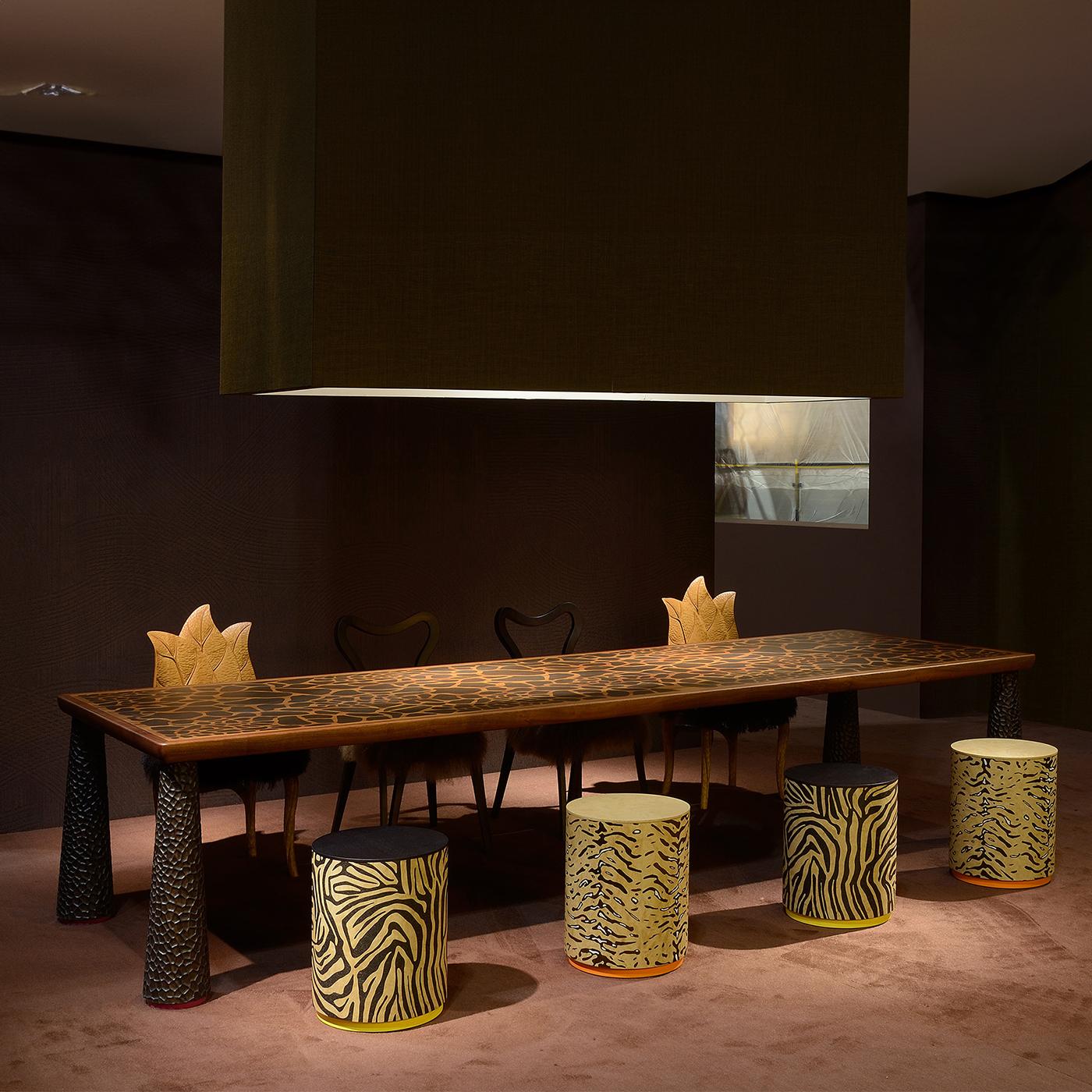 Un meraviglioso design dal carattere eclettico, questo sgabello cilindrico sarà il complemento perfetto per un interno rustico-chic. Realizzato a mano, si distingue per l'intarsio a strisce di tigre e la base laccata arancione che ne esalta il