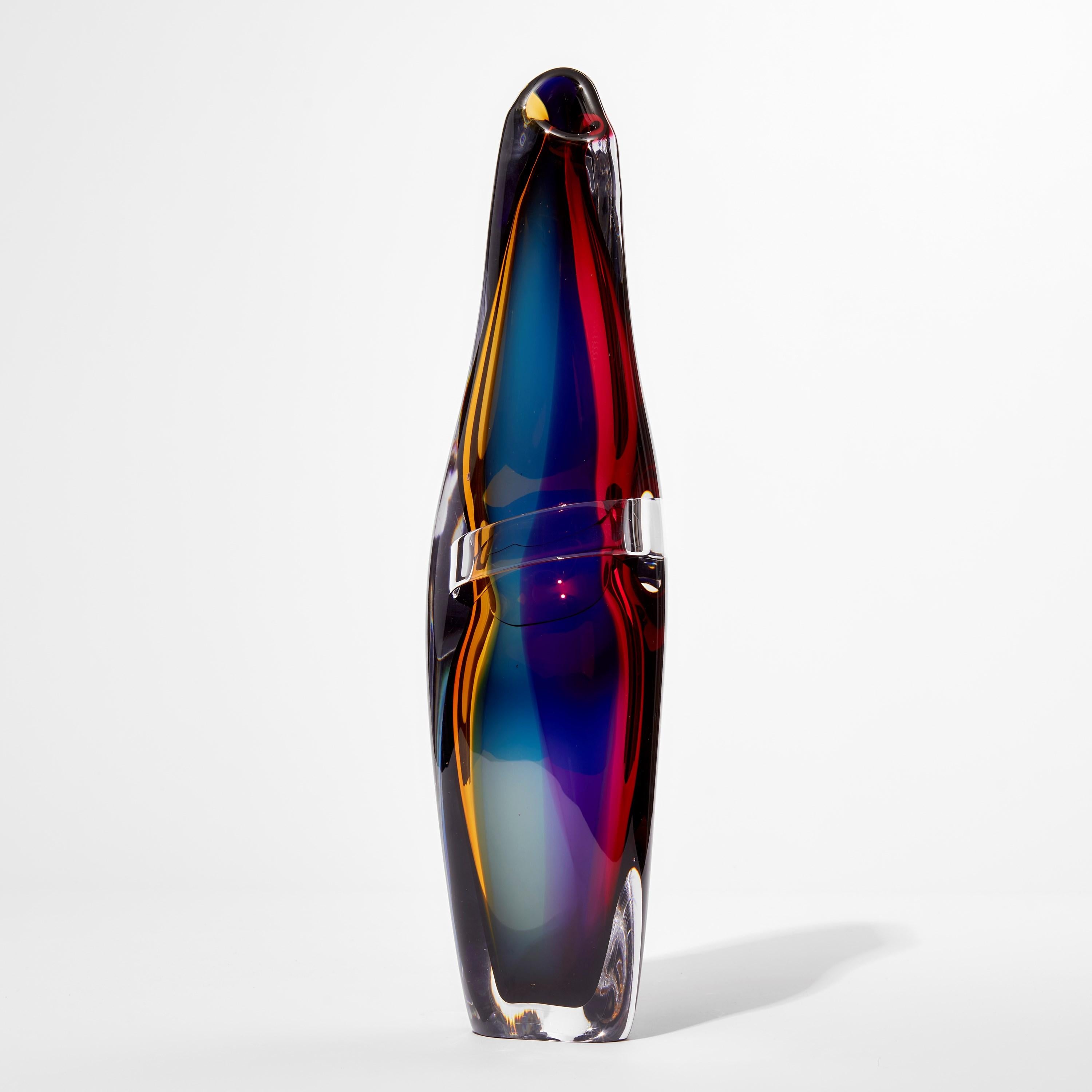 'Tricolarial 37' is a unique hand blown sculptural vase by the British artist Vic Bamforth. Blown in amber, red, purple and blue colored glass which are encased in clear glass to create this stunning piece. With soft, twisting lines, the form has