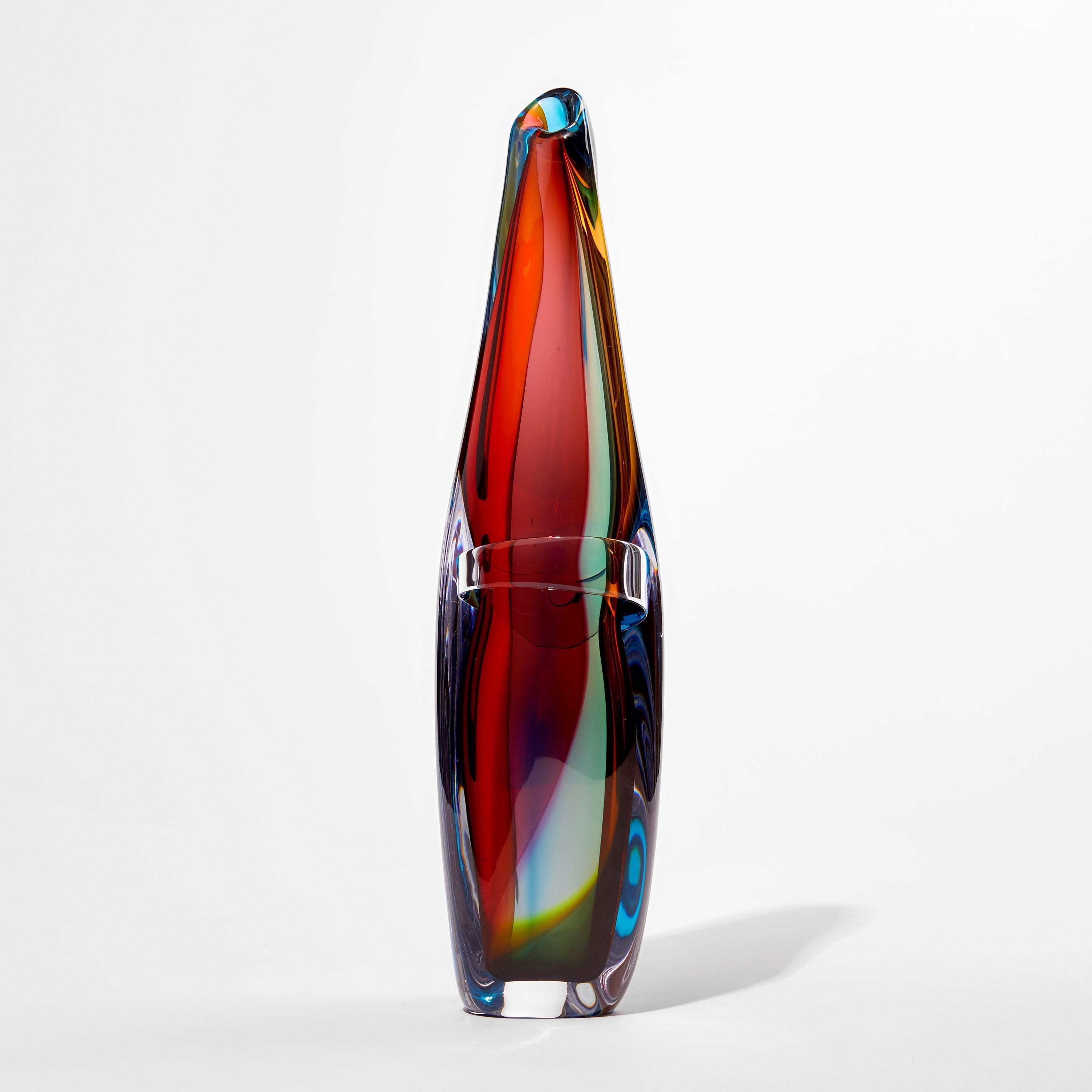 'Tricolarial 50' is a unique hand blown sculptural vase by the British artist Vic Bamforth. Blown in red, purple, blue and green colored glass which are encased in clear glass to create this stunning piece. With soft, twisting lines, the form has