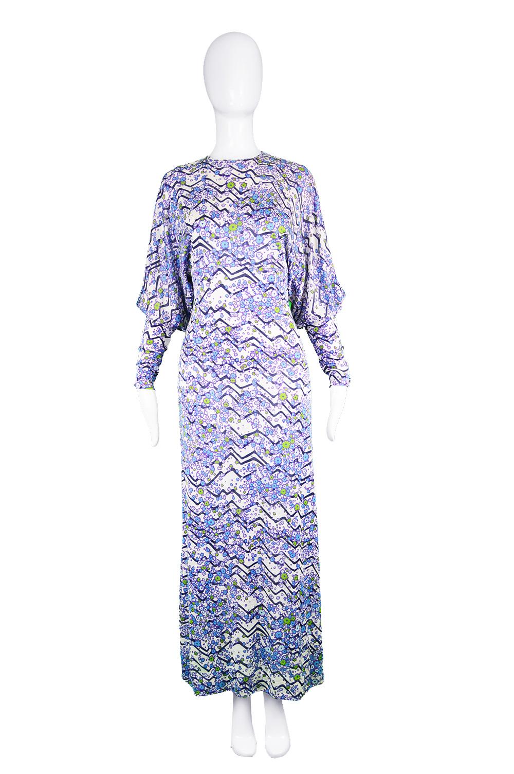 A fabulous vintage women's long dress from the 70s by luxury French label, Tricosa Paris. In a white synthetic jersey knit with a blue, green and purple floral pattern throughout. The batwing / dolman sleeves end in a long, fitted cuff creating a