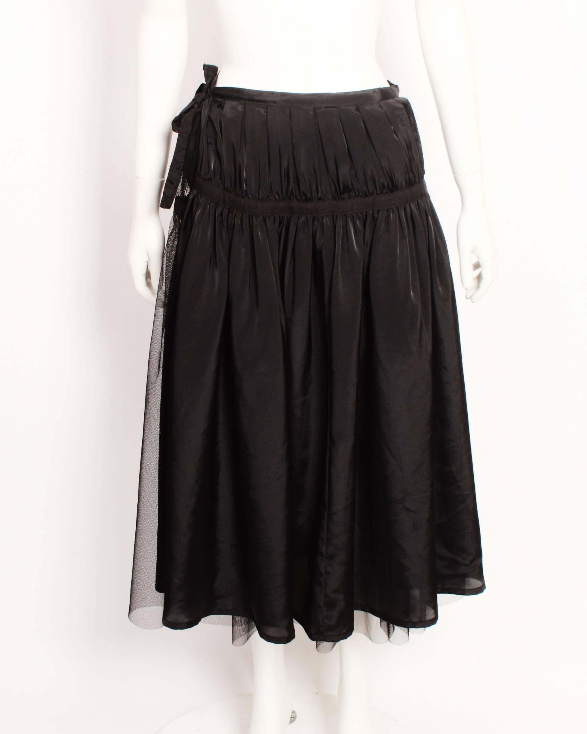 Tricot by Comme Des Garcons black tulle wrap skirt features a net skirt and solid underskirt that zip together. The silhouette is full and gathered with strips of of cotton tape that run around the waist and hipline. These hold the gathers in place