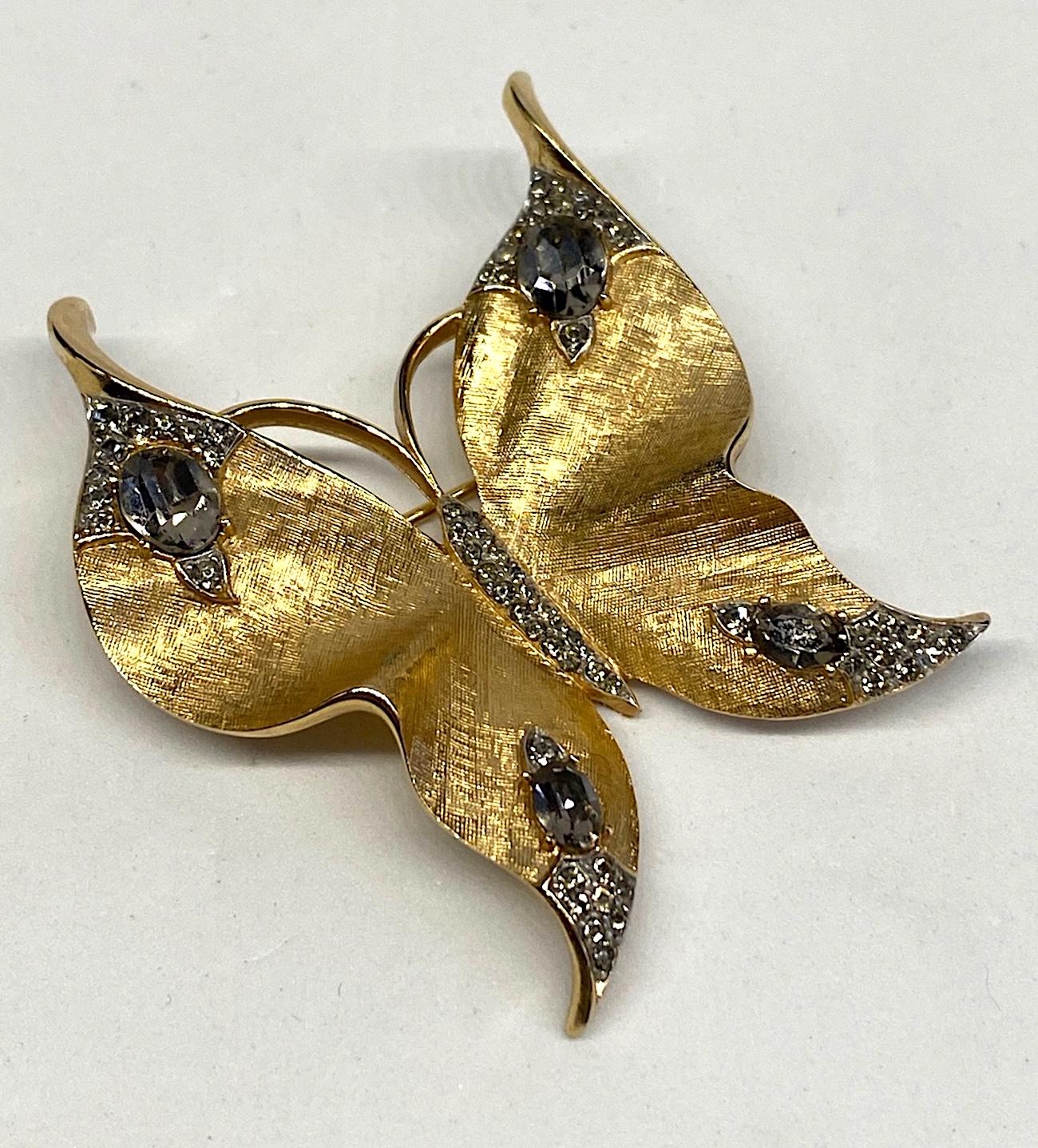 A lovely Trifari butterfly brooch from the 1950s. The wing are in a textured satin gold while the edges and tips are a shiny gold for contrast. A large oval grey rhinestone at the top of each wing and mirrored with a small oval grey rhinestone on