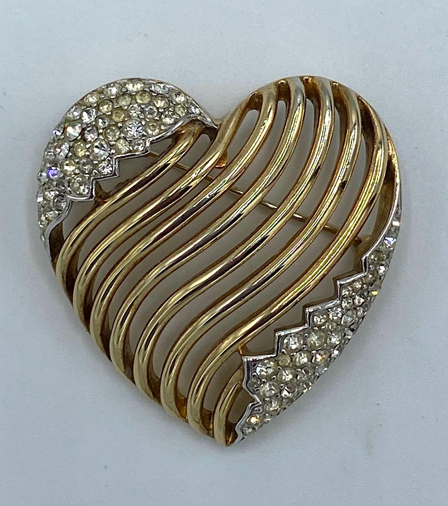 A vintage openwork gold heart pin with rhinestone accents from famed American fashion jewelry company Trifari. The design for this brooch was patented in 1953. The brooch is lightly domed with curved bars running diagonally and pave' set rhinestones