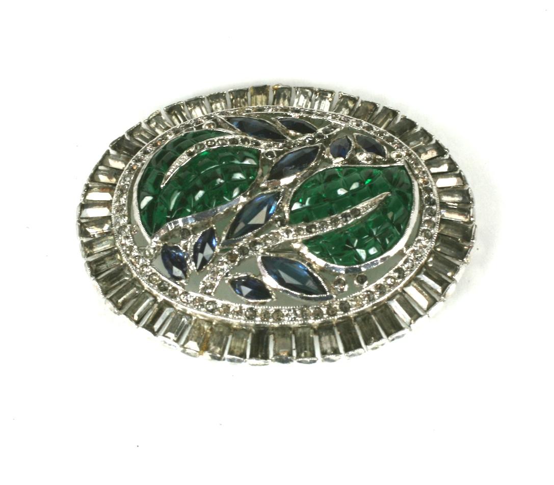 Trifari Alfred Philippe KTF rare invisibly set oval brooch. In an Art Deco design of  invisibly set faux emerald glass leaves and sapphire marquise vines. Set with pave crystals, and a surround of rectangular baguettes in rhodium metal.
Excellent