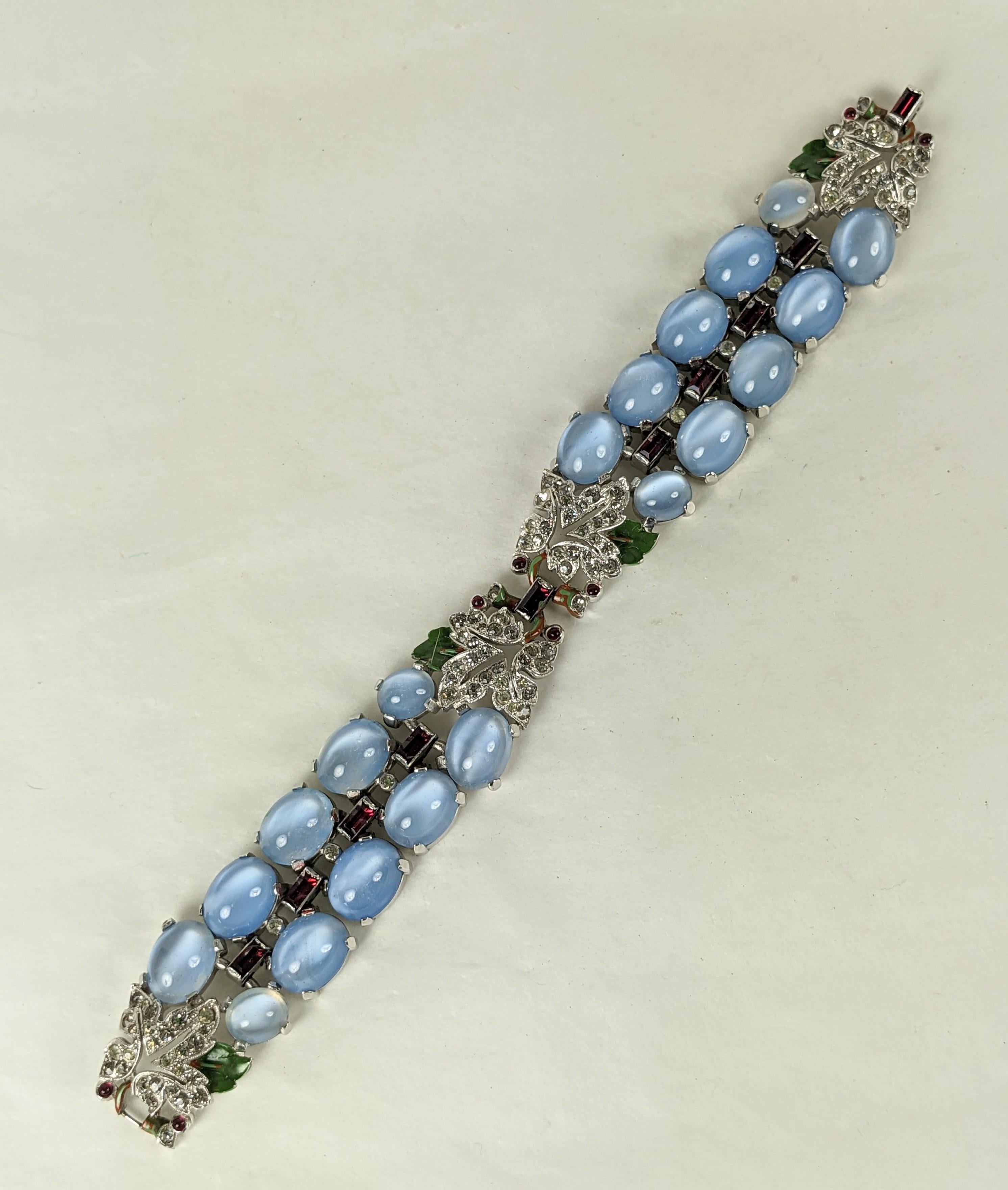 Rare and collectible Trifari Blue Moonstone Ruby and Enamel Deco Bracelet by Alfred Phillipe. 2 rows of oval faux blue moonstones are accented with enamel, ruby baguettes and cabs within pave rhinestone leaves. Rare original enameling. 1930's USA.