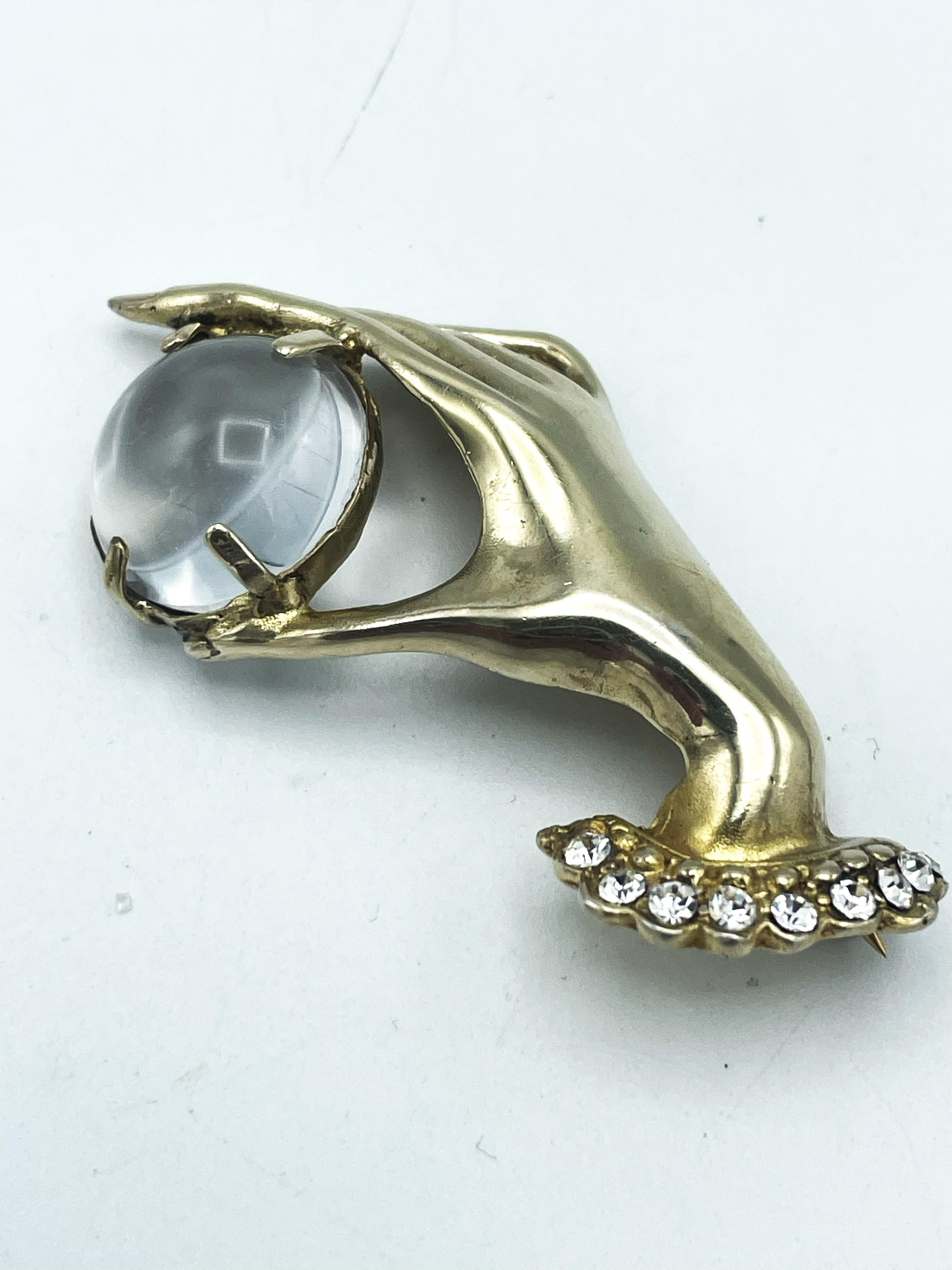 A brooch in the shape of an elegant, slender hand holding a Jelly Belly ball between thumb and forefinger. Below the wrist there is a ruffle decorated with rhinestones. 
Measurement
Brooch width 6 cm  Height 3 cm. Deep 1 cm 

Features
- Signed