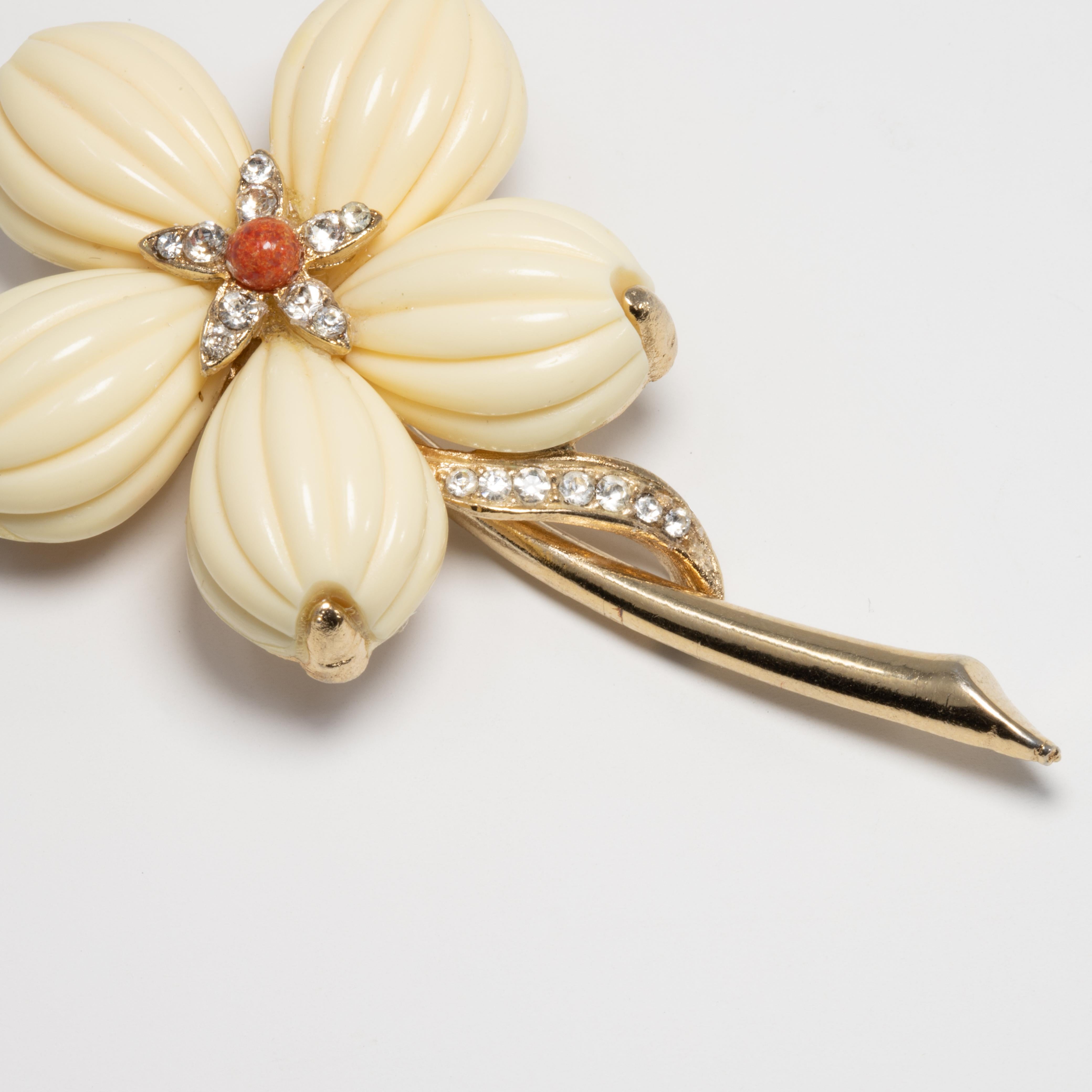 A classy Trifari brooch/pin. This pretty flower features cream-colored carved lucite petals prong set in the signature Trifari textured gold filled metal setting. The flower is also accented with clear crystals and a single faux coral