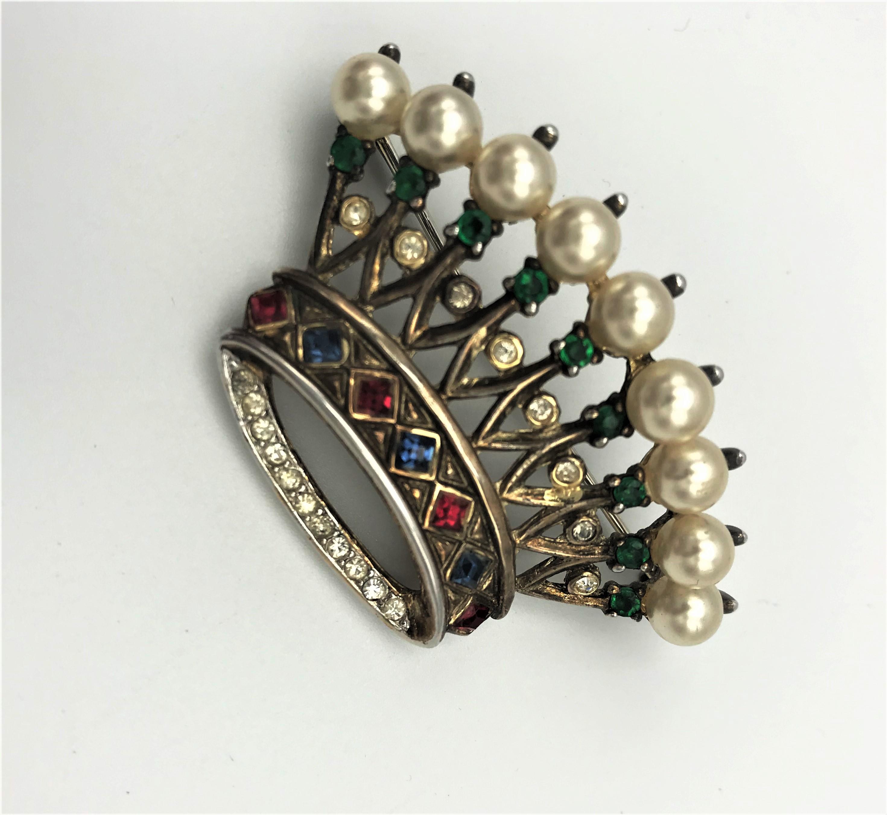 Trifari crown brooch of vermeil sterling with emerald green ruby red, and clear rhinestones, and a ring of faux pearls. 1940s
Measurement: 5 cm (2 