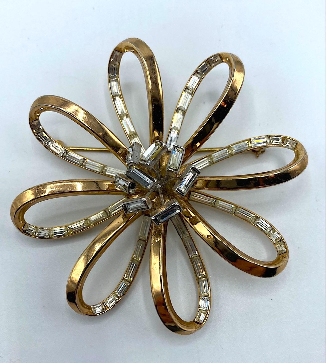 A wonderful and three dimensional 1940s flower brooch by renowned American costume jewelry company Trifari. Each of the flower petals is designed as an open loop shape. The rhinestone baguettes are set on the inside back of the petal. The solid gold